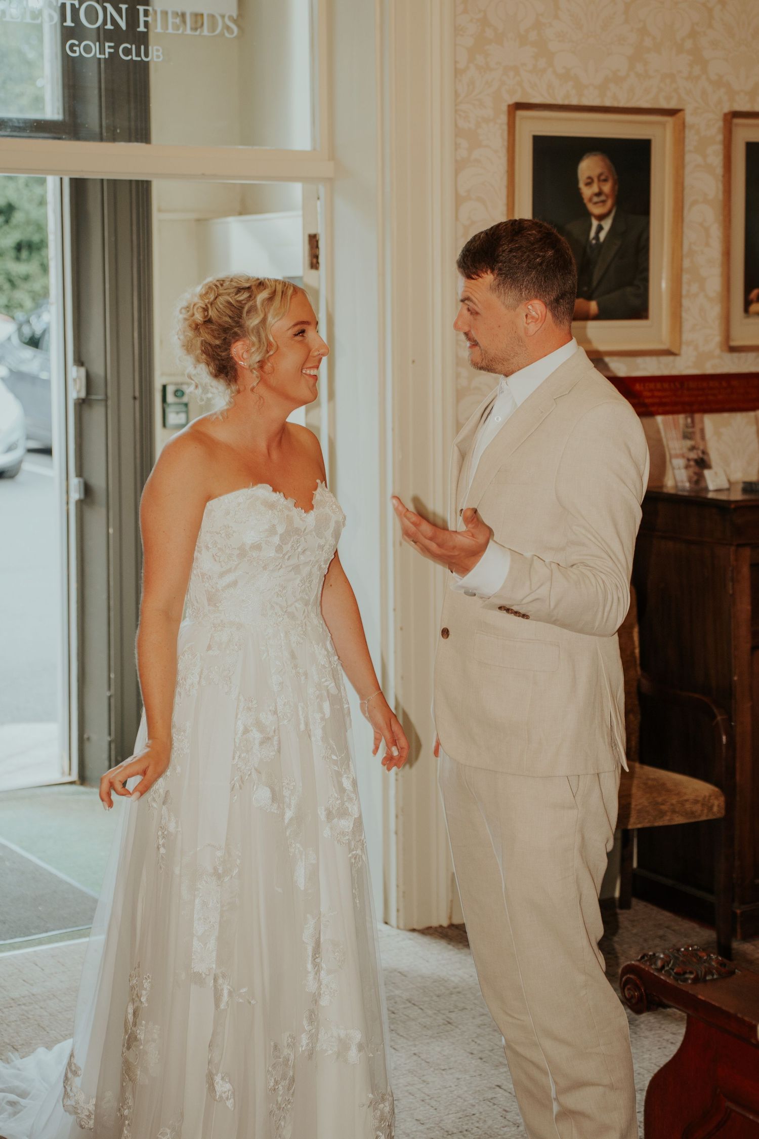 Bride in strapless lace gown and groom in cream suit share a joyful first look moment at a golf club venue.