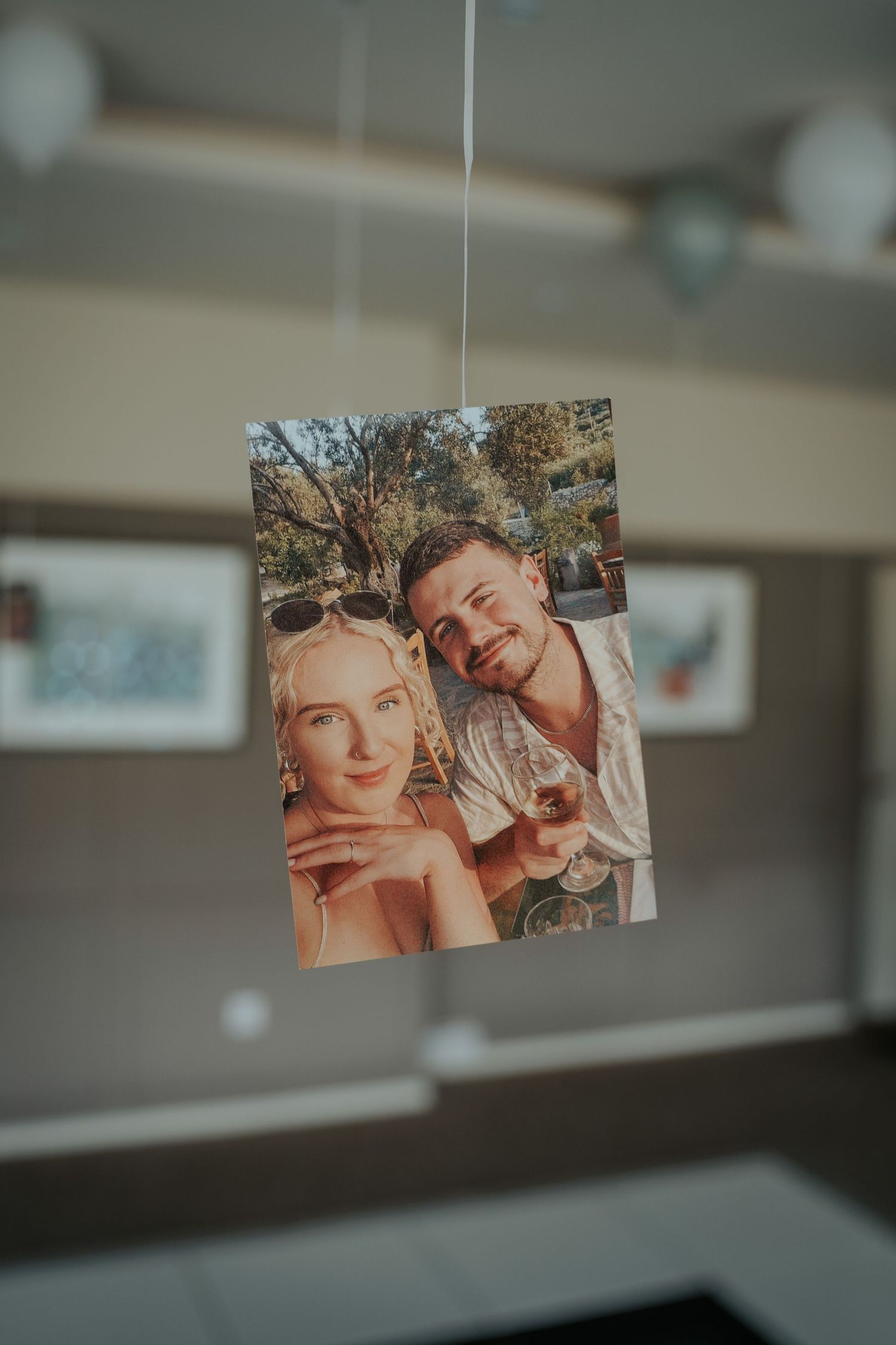 A printed photo of a smiling couple taking a selfie outdoors, hanging from a string in a modern gallery space.