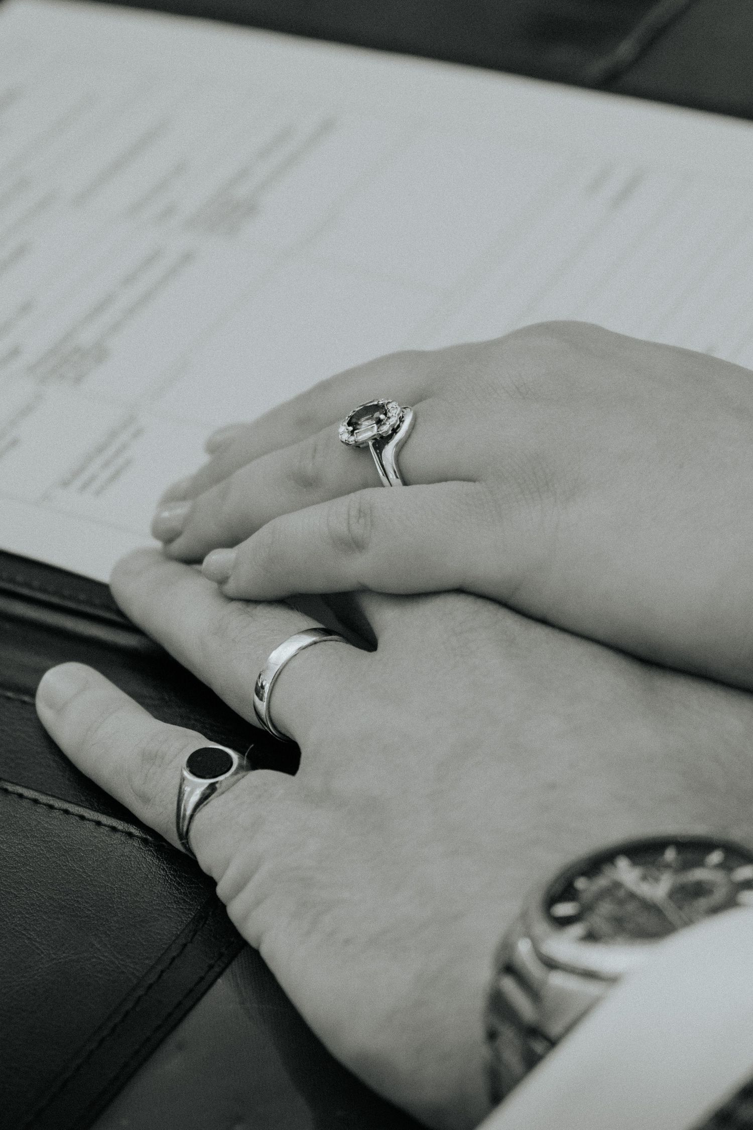 Black and white photo of two hands with wedding rings resting on a marriage certificate document.