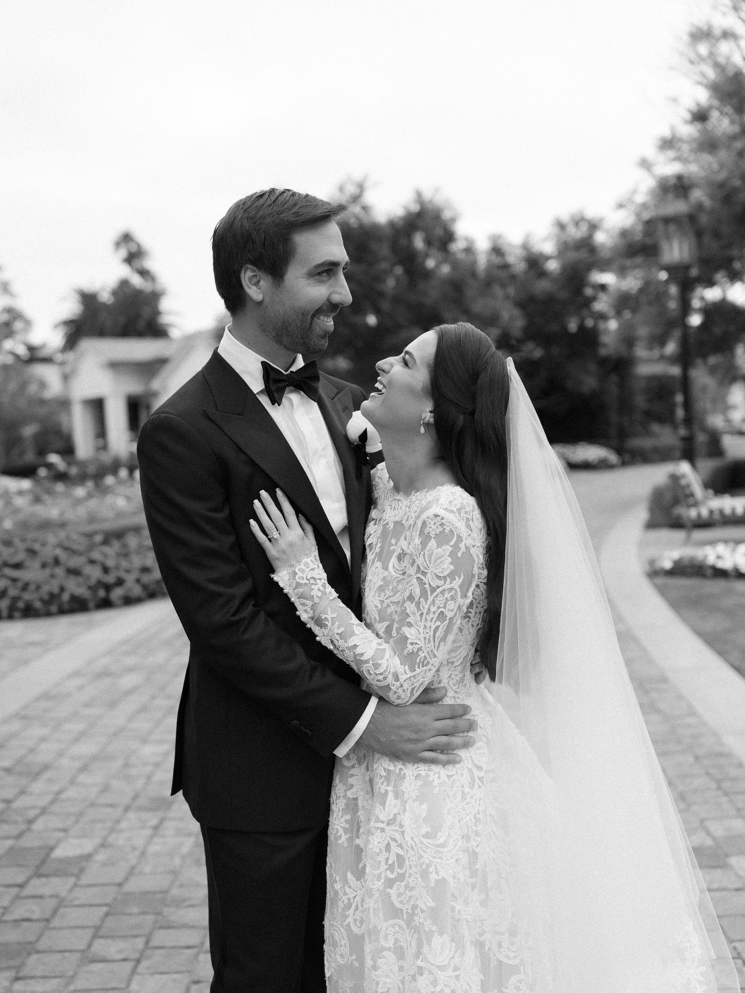 Black and white portrait of smiling bride and groom embracing at outdoor wedding venue.