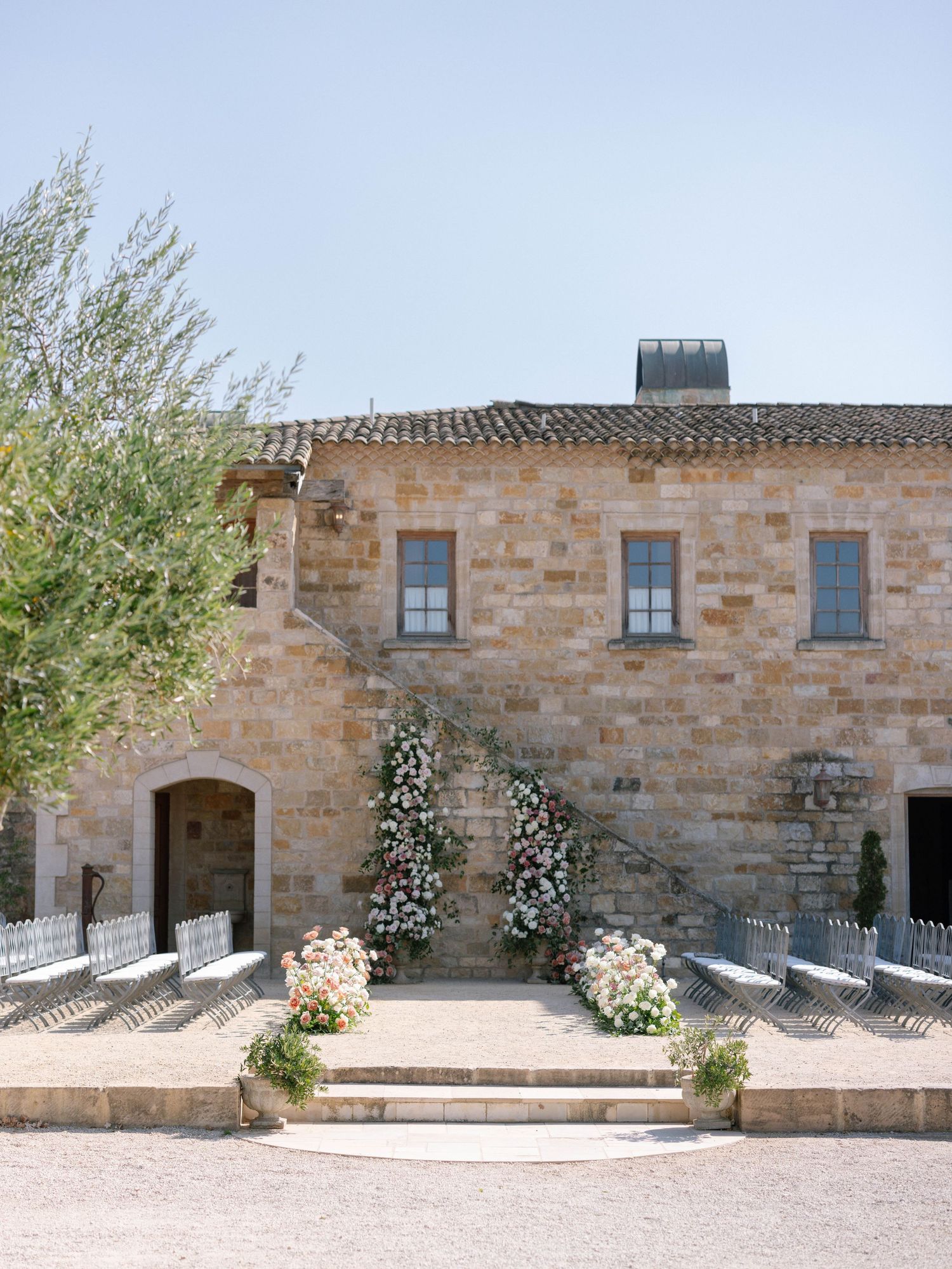 Rustic stone wedding venue exterior adorned with floral arch and white ceremony chairs.