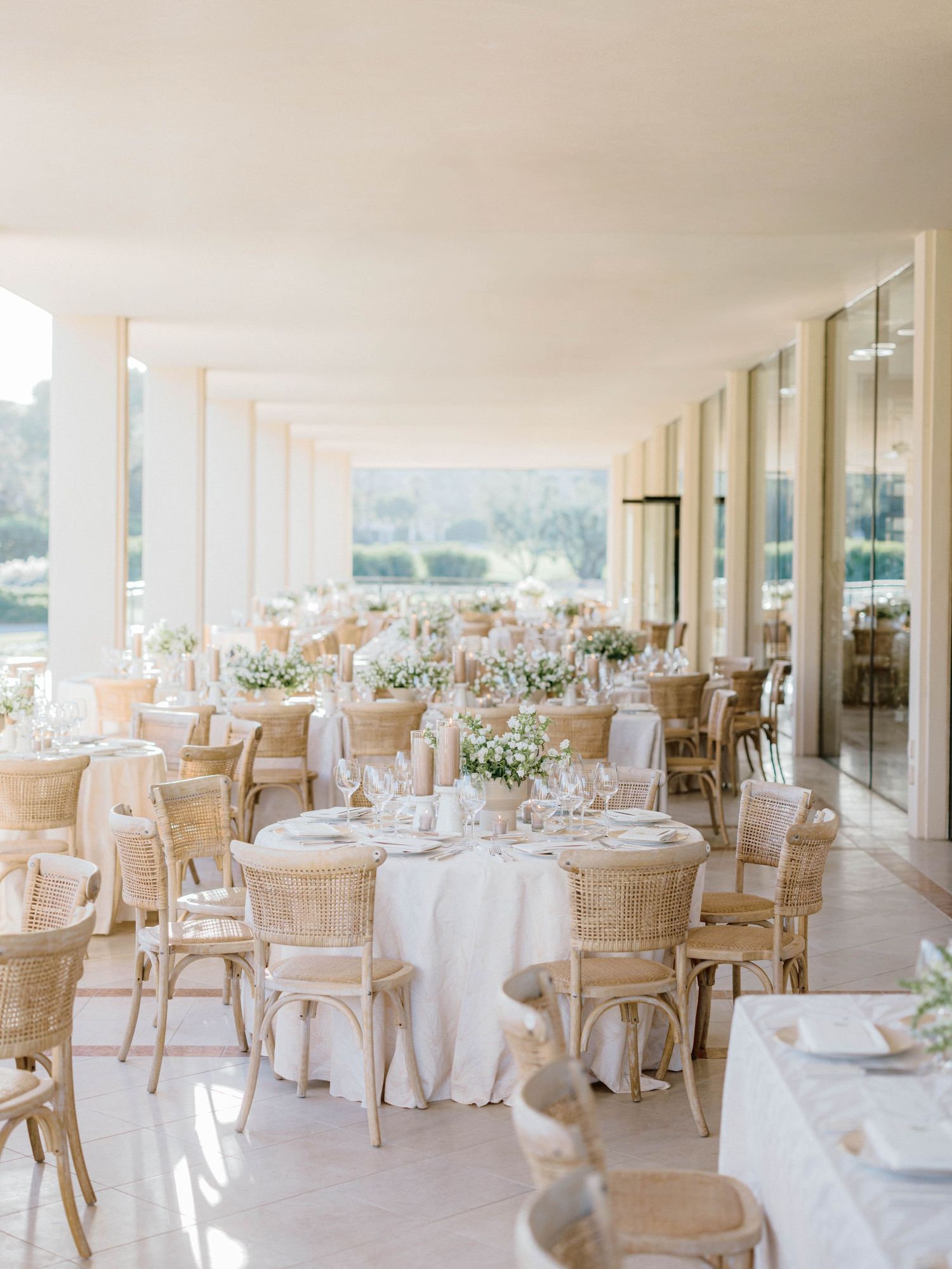 Elegant outdoor wedding reception with white linen tables, rattan chairs, and floral centerpieces.