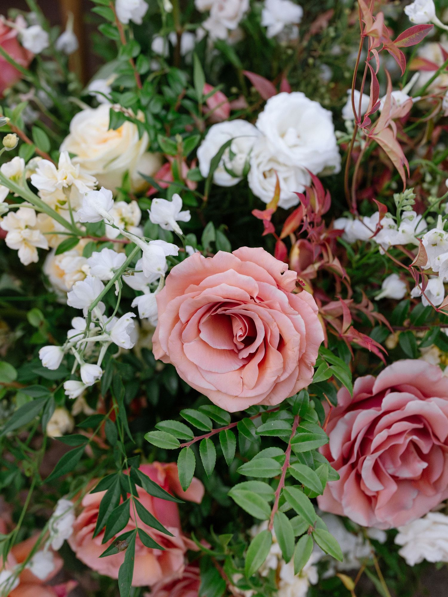 Close-up of elegant wedding floral arrangement featuring blush pink roses, white blooms, and lush greenery.