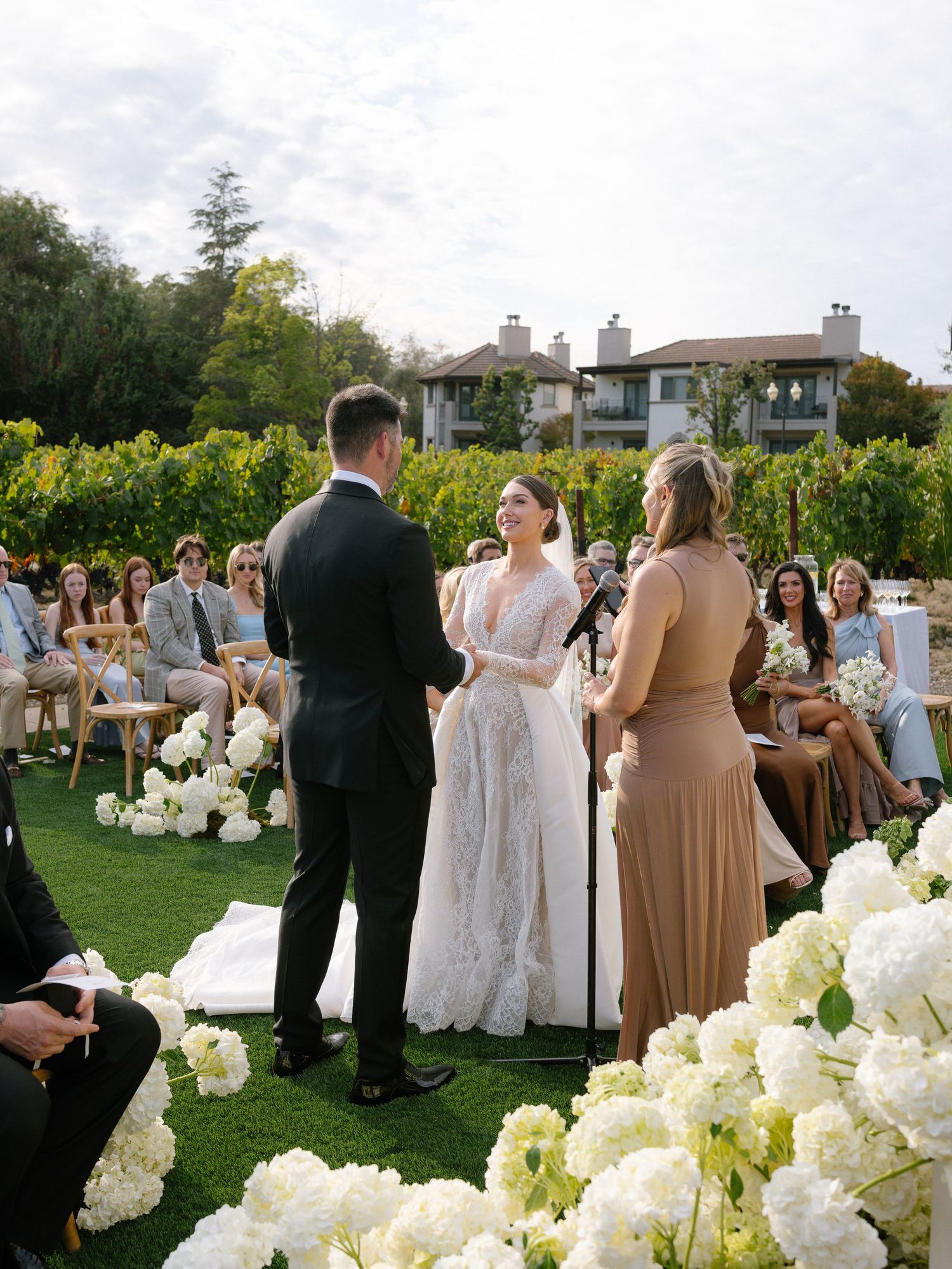 Bride and groom exchanging vows at outdoor vineyard wedding ceremony lined with white hydrangeas.