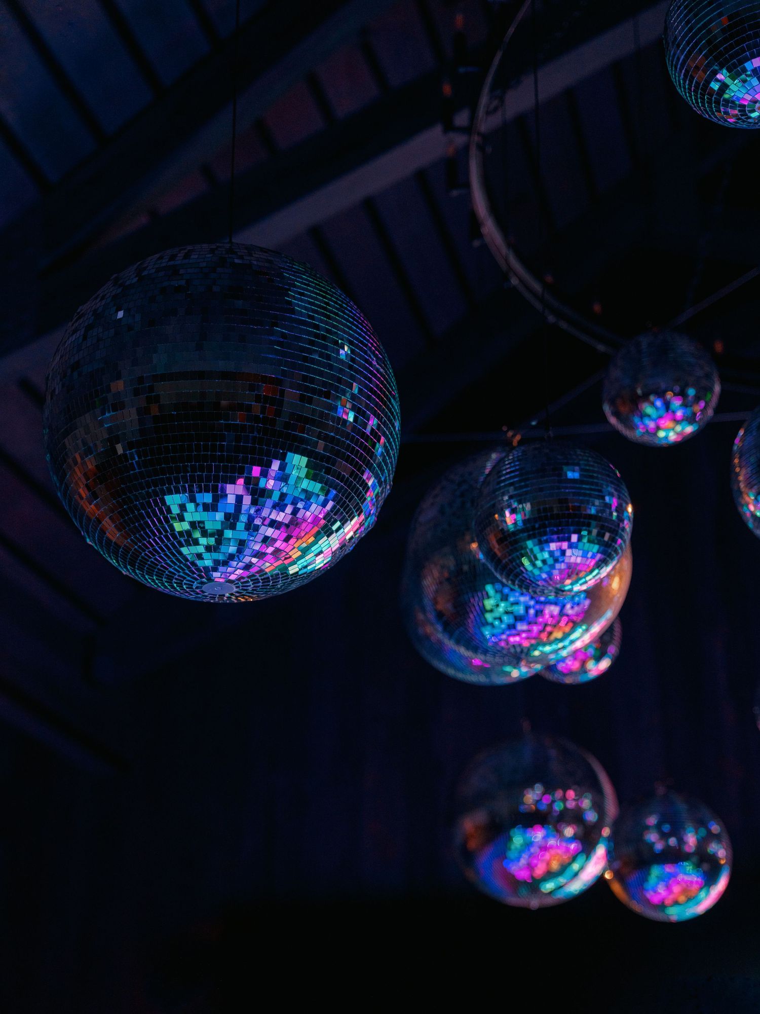 Colorful disco mirror balls hanging from dark ceiling at a wedding reception.