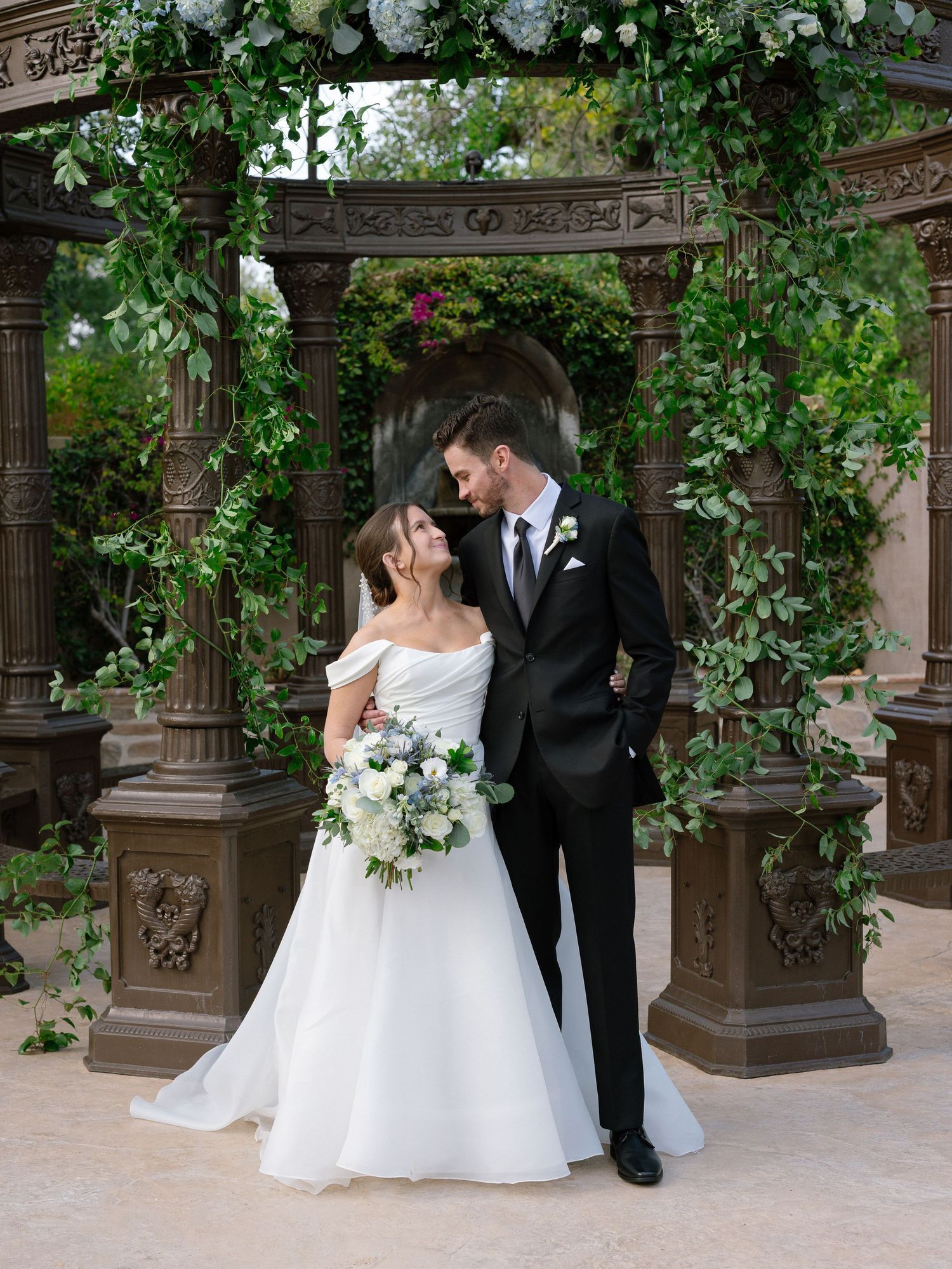 Bride and groom share a romantic moment under a floral arch with lush greenery at their wedding at Westlake Village Inn in Westlake Village.