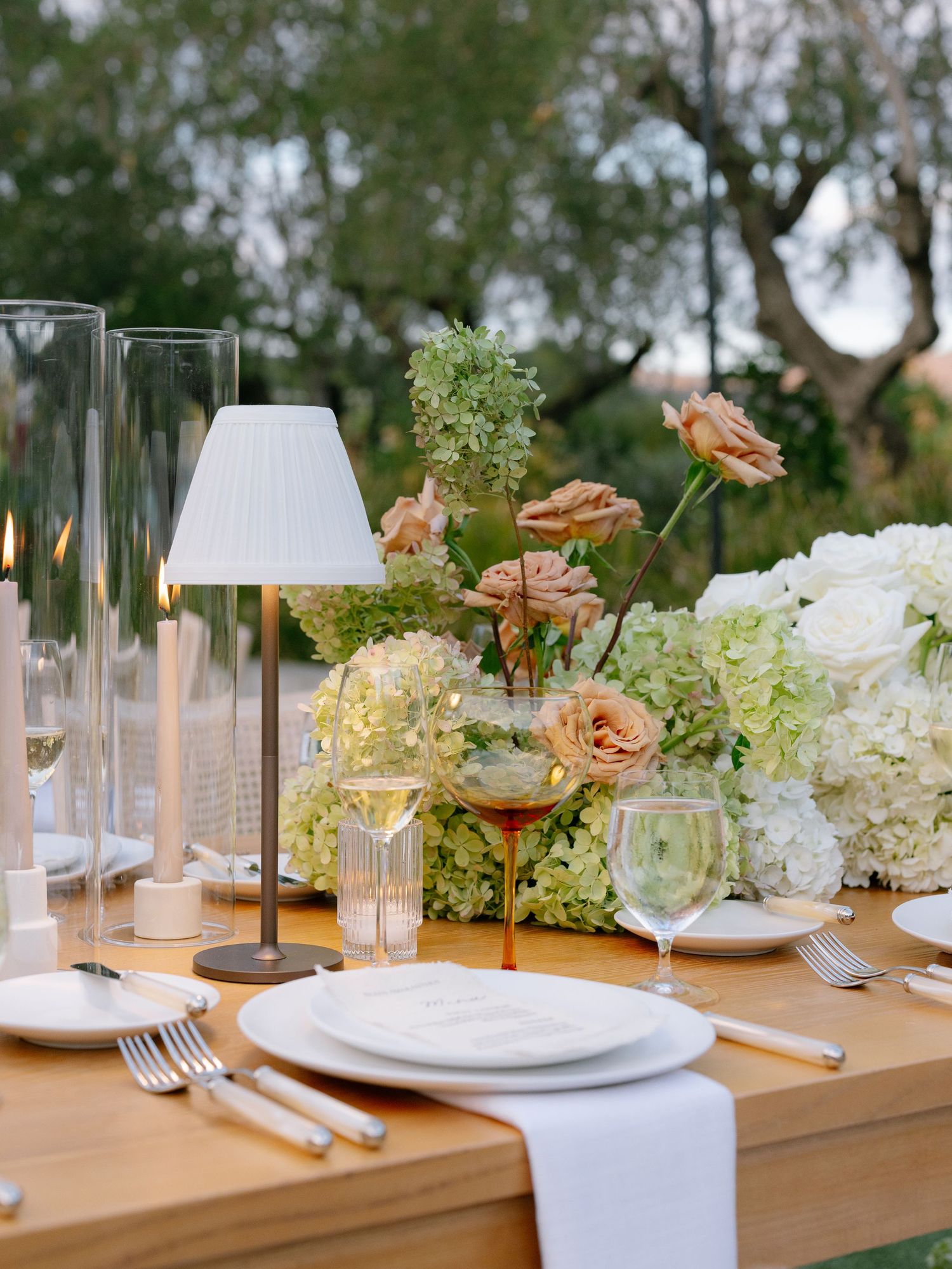 Outdoor wedding table with white hydrangeas, peach roses, and modern lamp centerpiece.