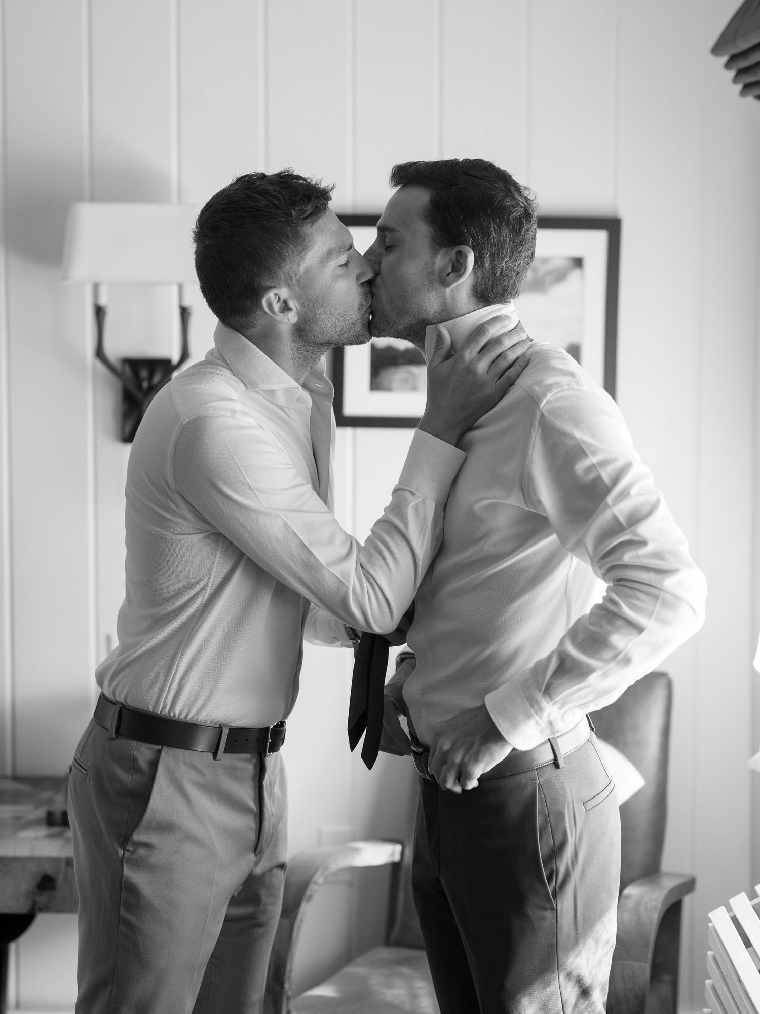 Two grooms share a romantic kiss while getting ready on their wedding day indoors.