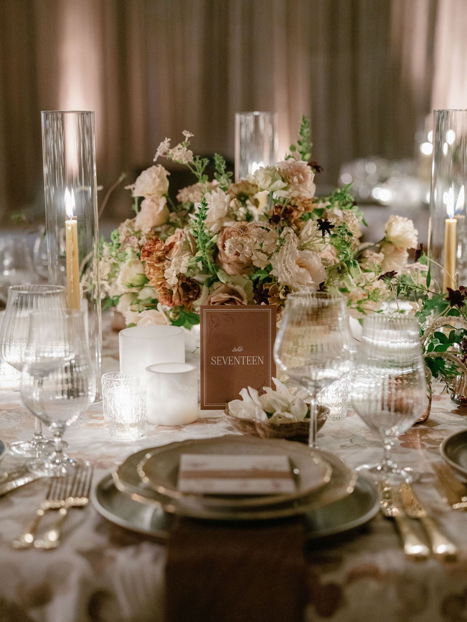 Elegant wedding table setting with blush floral centerpiece, gold candlesticks, and crystal glassware at table seventeen.