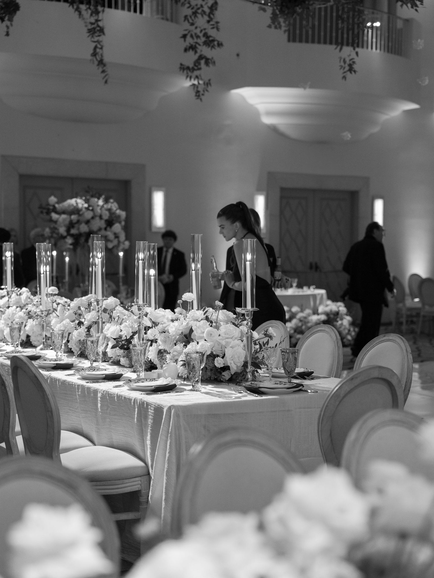 Black and white photo of a wedding reception table set with candles, florals, and elegant place settings.