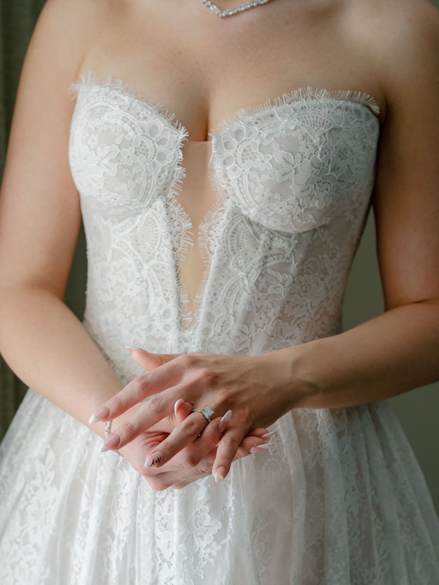 Close-up of bride in strapless lace corset wedding gown with hands clasped showing engagement ring.