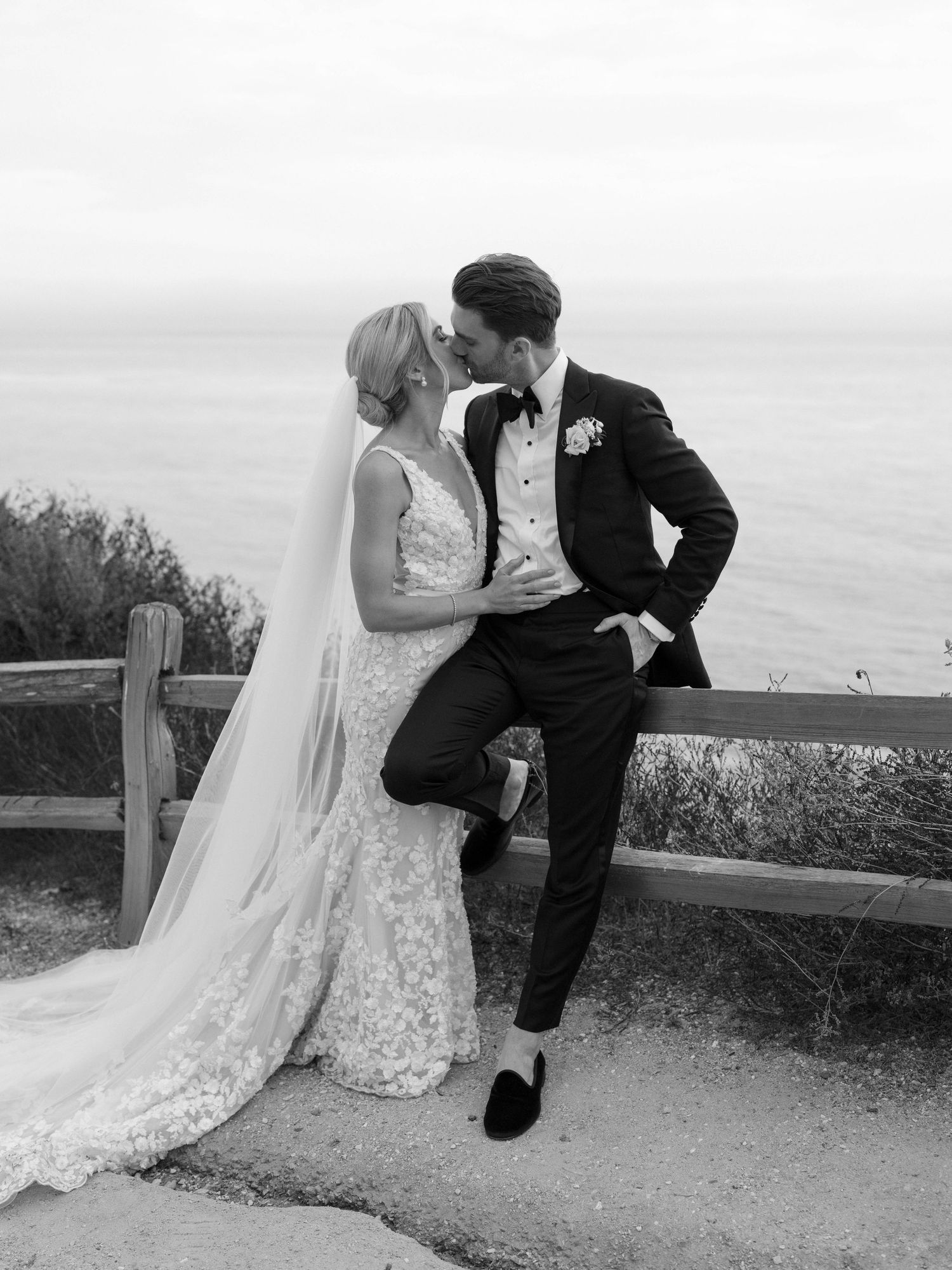 Black and white photo of bride and groom sharing a kiss on a coastal clifftop with ocean views.
