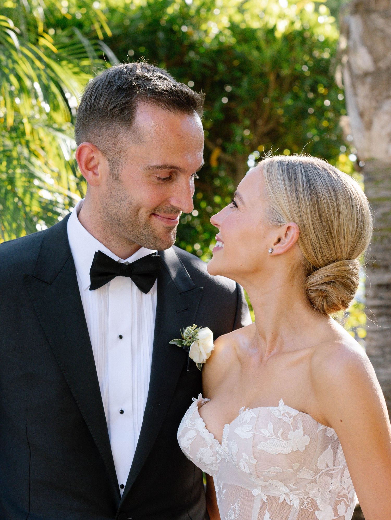 Smiling bride and groom in black tuxedo share an intimate moment at outdoor wedding.