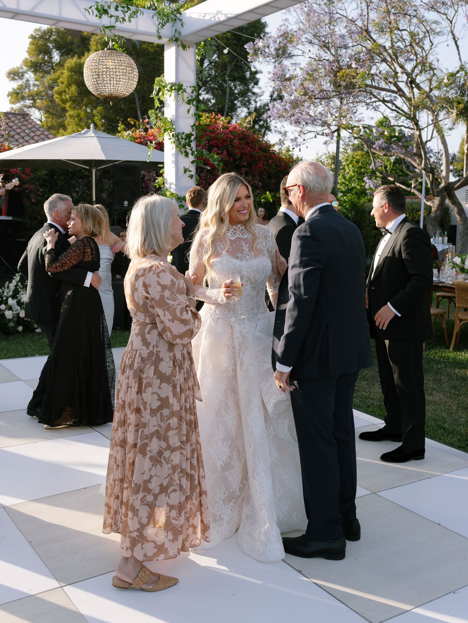 Bride in lace gown conversing with elderly guests on an outdoor wedding dance floor.