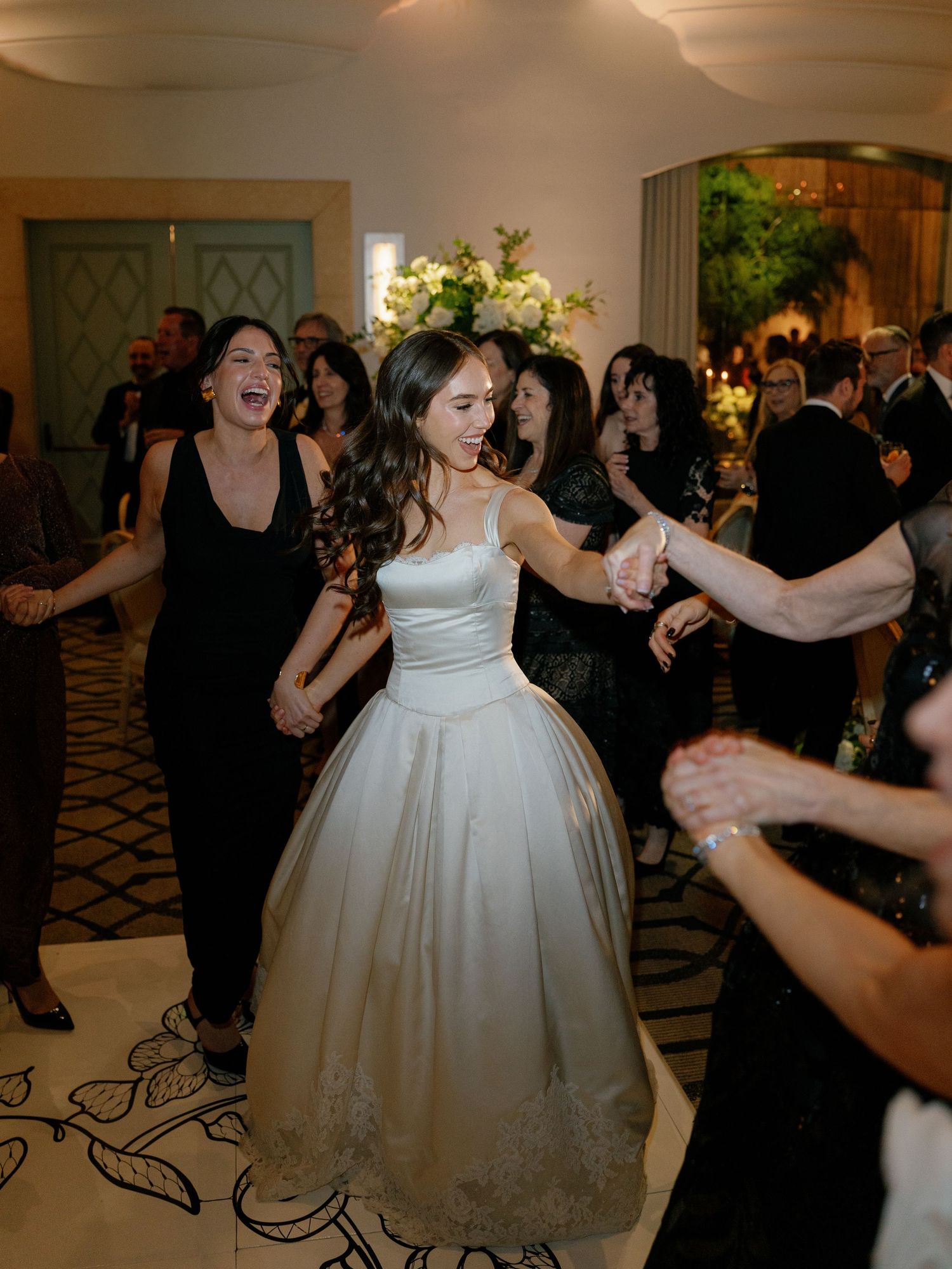 Bride in a white ball gown dancing joyfully with guests at her wedding reception.