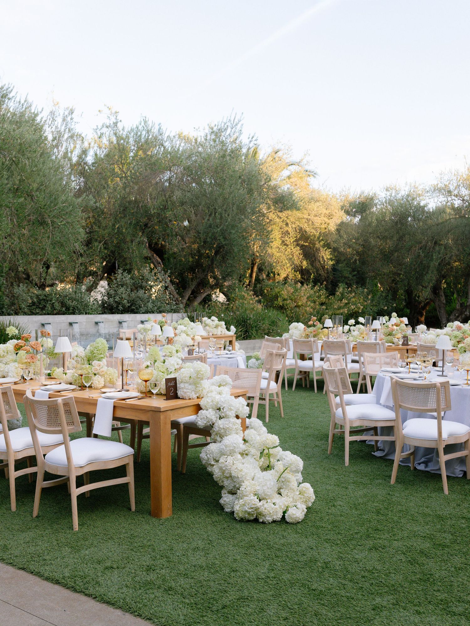 Elegant outdoor wedding reception with white floral garland centerpiece on green lawn.