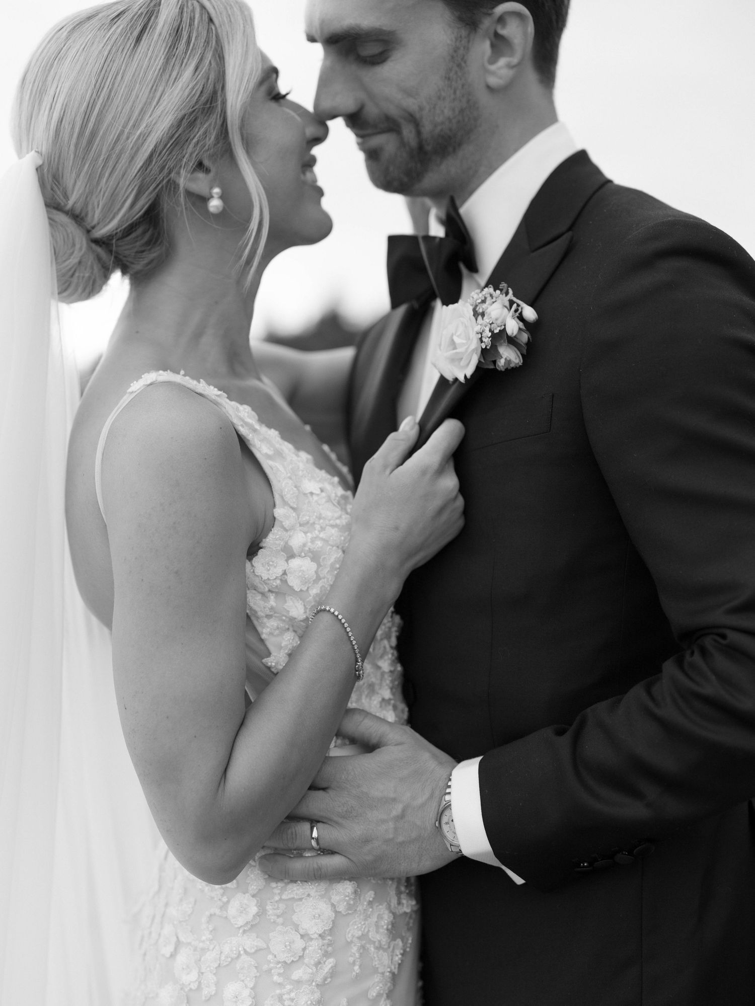 Black and white romantic portrait of bride and groom nearly kissing, bride in floral lace wedding gown.