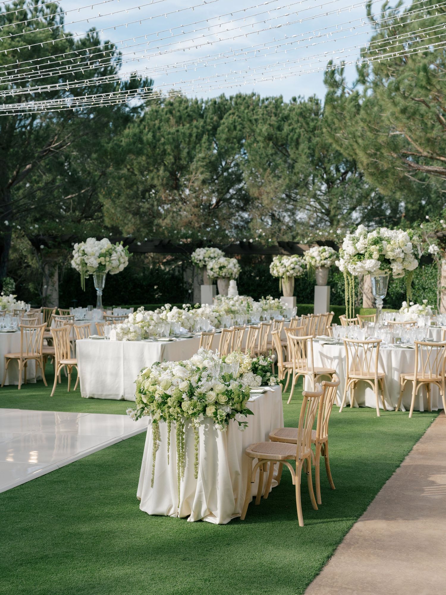 Elegant outdoor wedding reception with white floral centerpieces, gold chairs, and string lights.