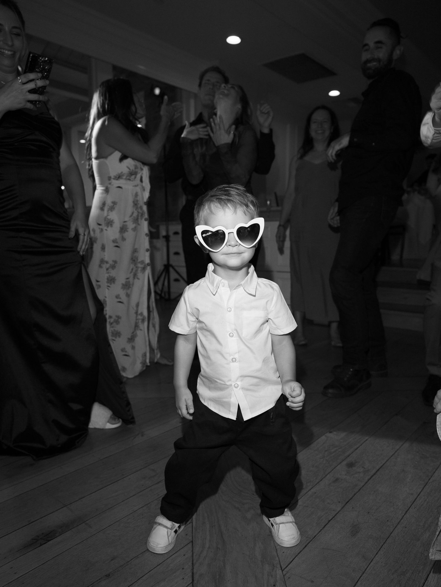 Adorable young boy wearing heart-shaped sunglasses dances on the wedding reception dance floor.