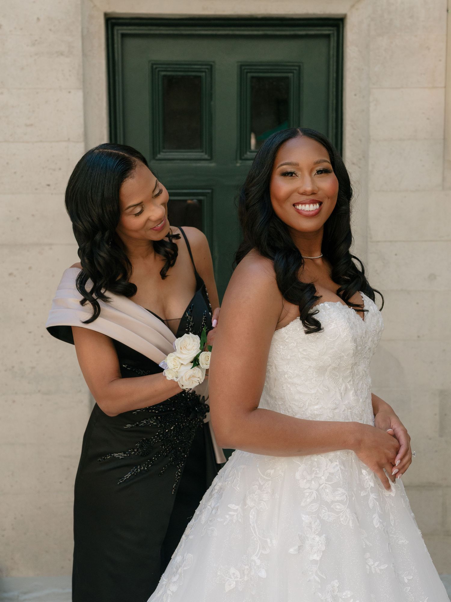 Bride in white strapless gown poses with bridesmaid in black dress before green door.