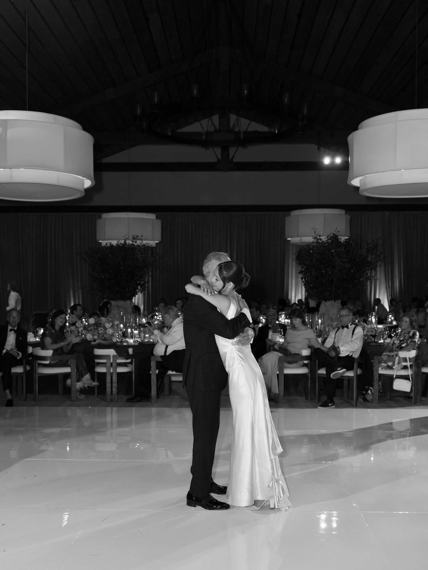 Bride and groom share first dance in elegant black and white wedding reception photo.