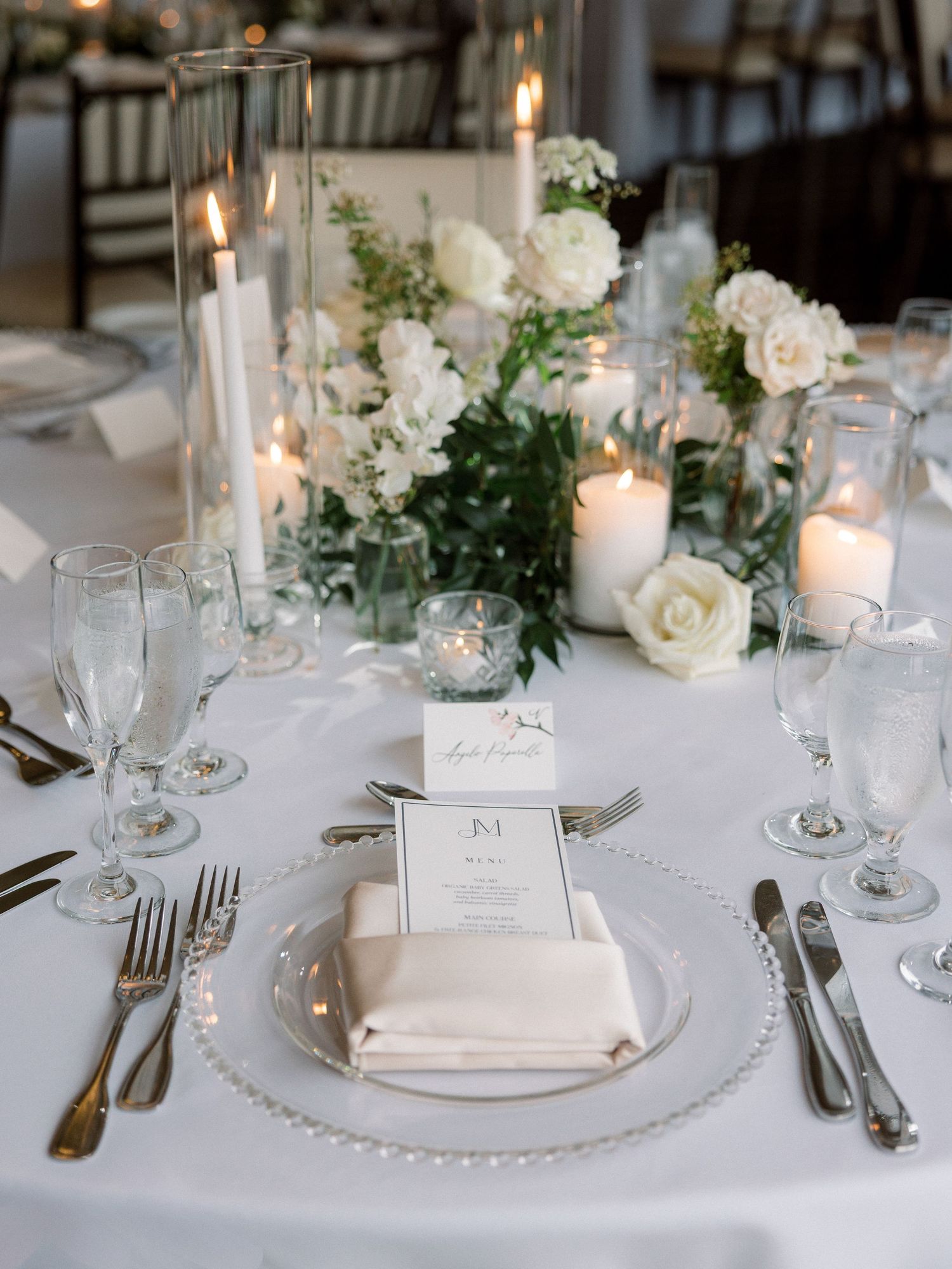 Classic white wedding place setting with pearl charger, menu card, and floral centerpiece.