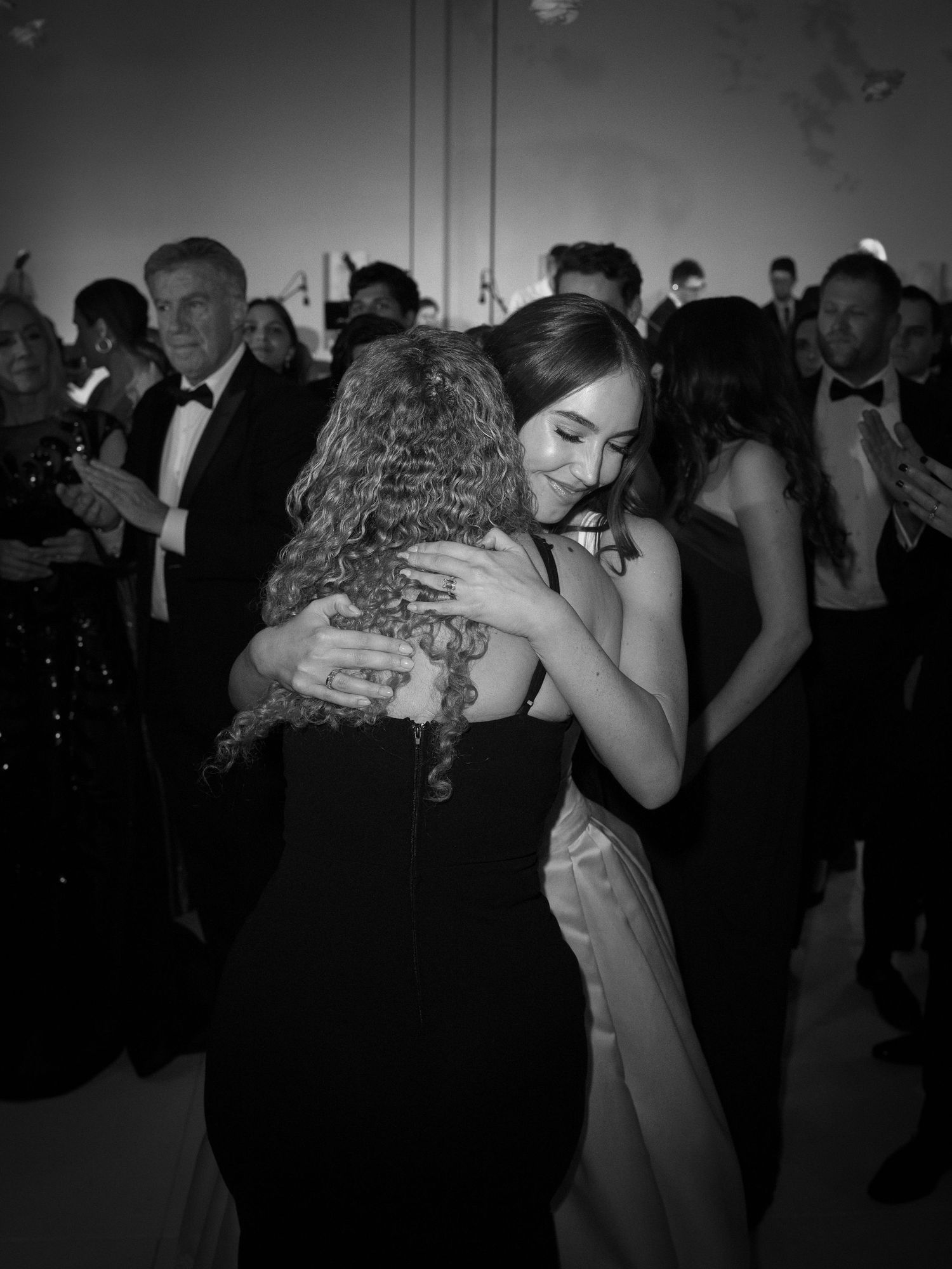 Black and white photo of bride sharing emotional hug with guest on wedding dance floor.