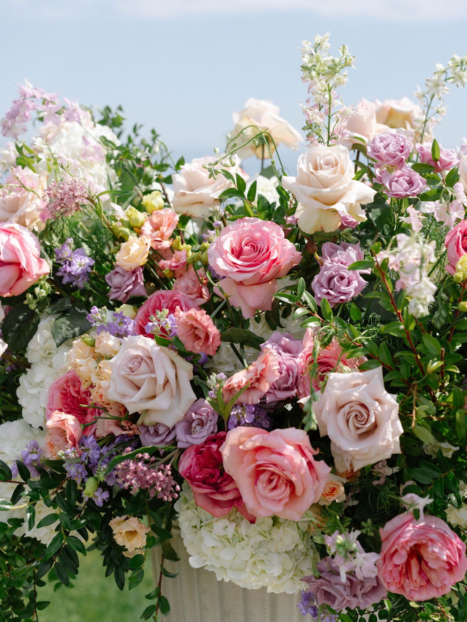 Close-up of stunning wedding floral arrangement with pink, blush, and white roses against a blue sky backdrop.