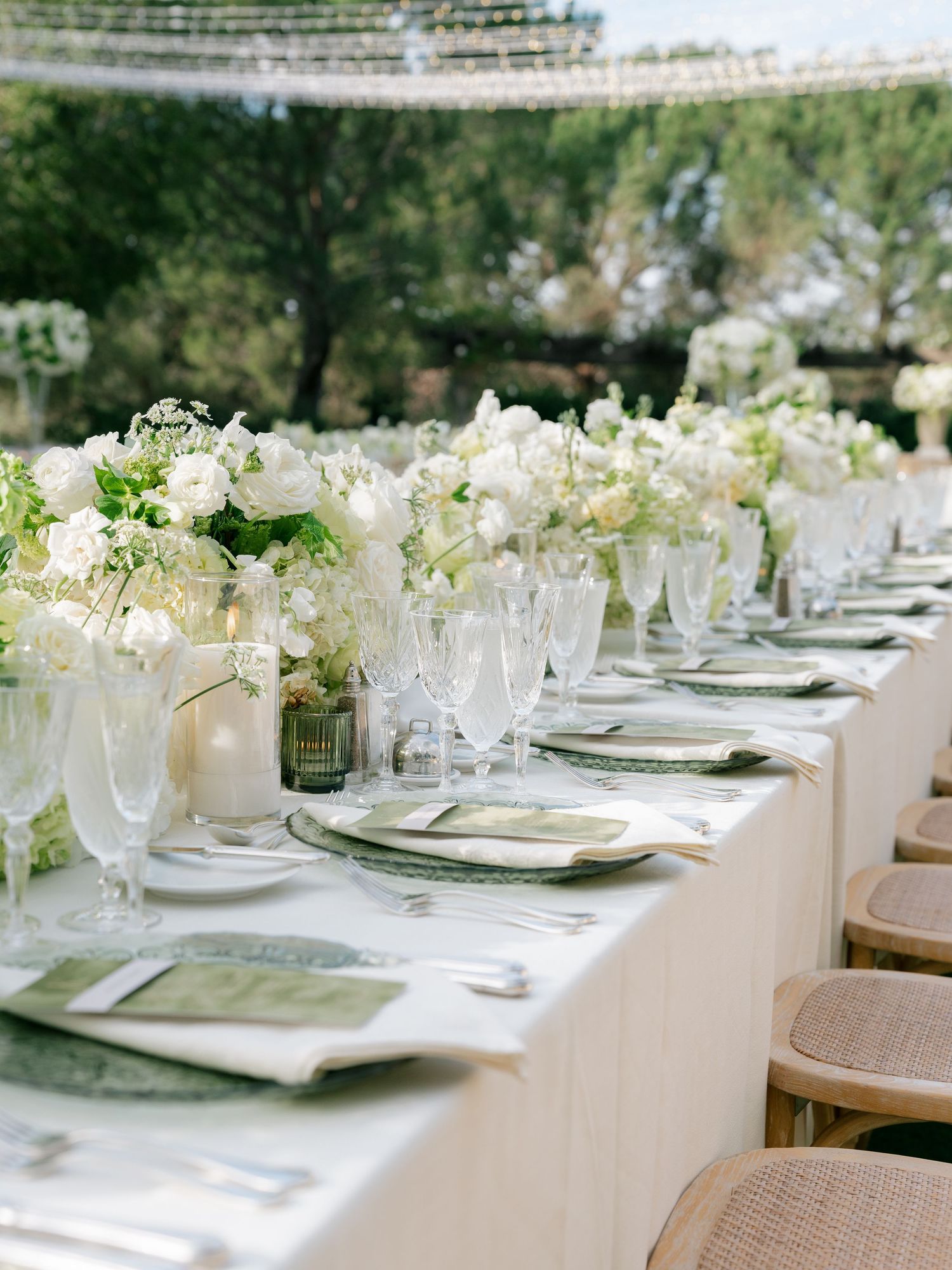Luxurious wedding tablescape with white floral arrangements, crystal glassware, and green chargers.