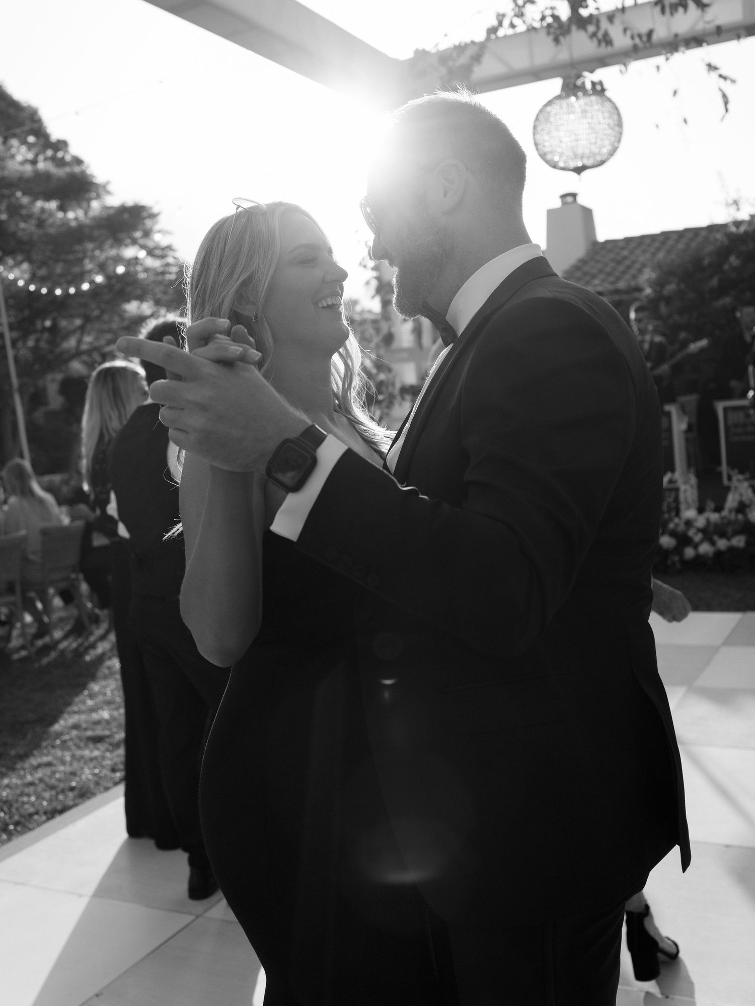 Couple sharing a romantic dance backlit by golden sunset glow at outdoor wedding reception.