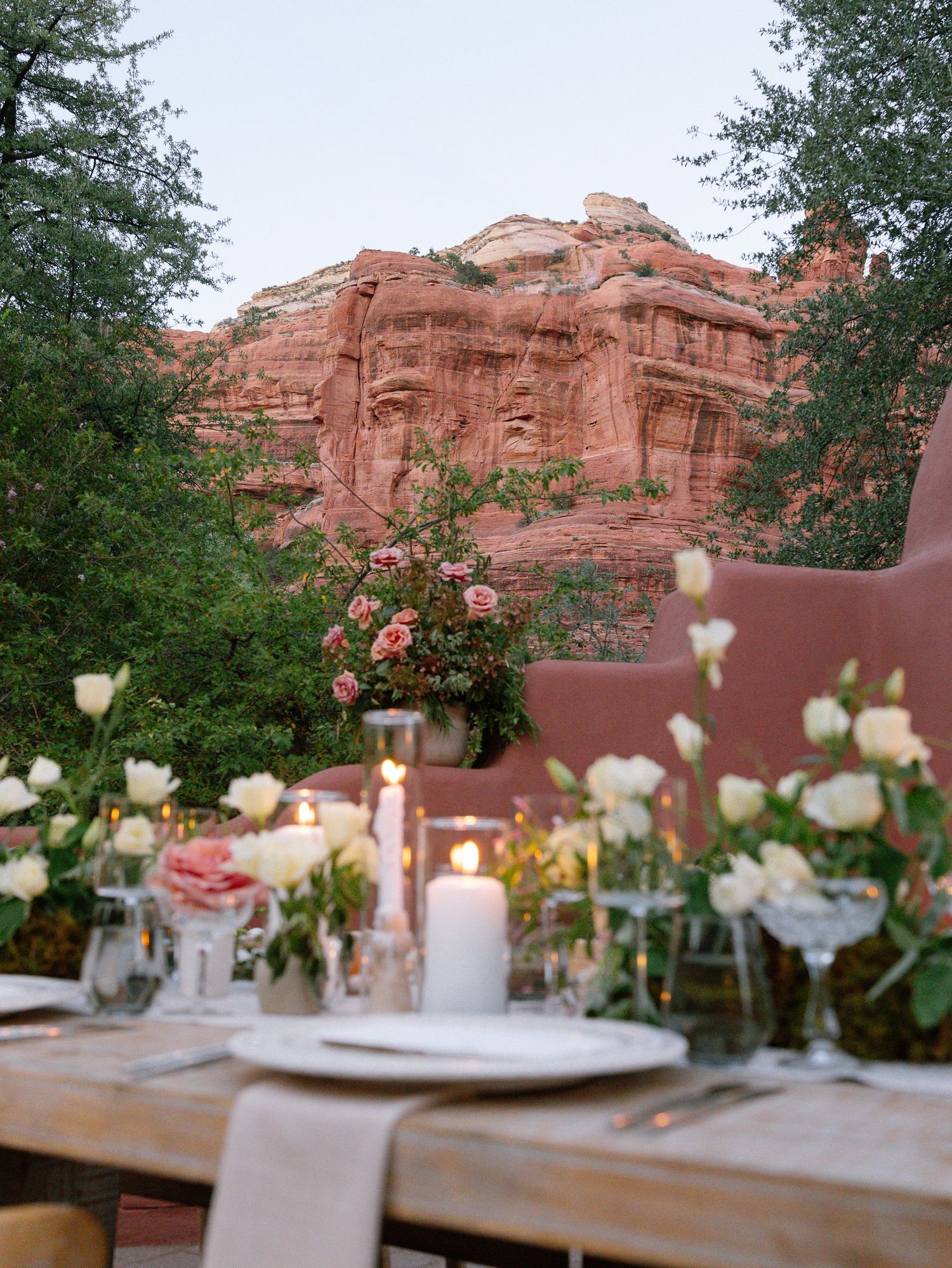 Romantic outdoor dinner table with candles and roses set against stunning red rock formations in Sedona at dusk.