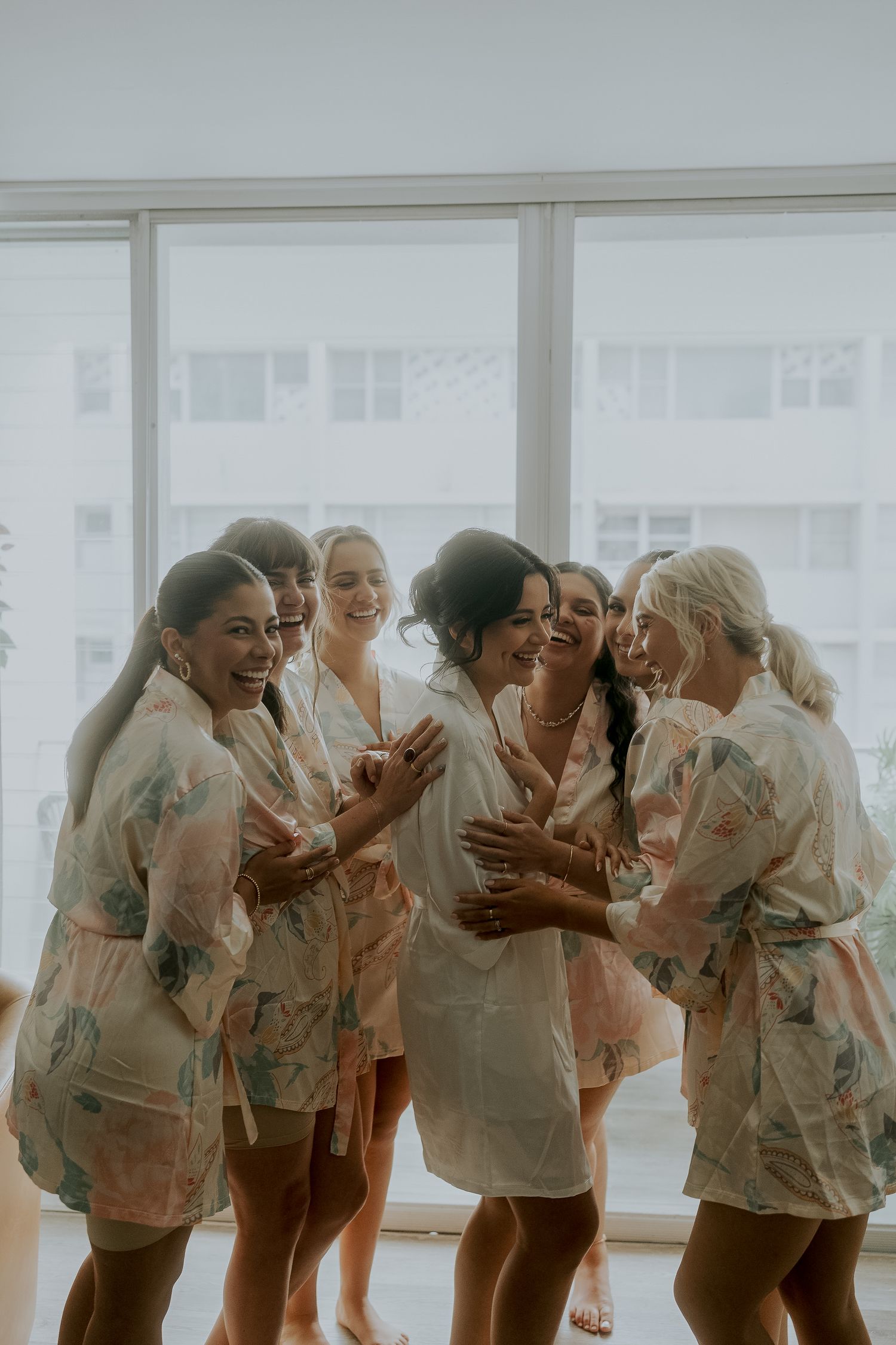 Bridesmaids laughing together in matching floral robes during wedding morning preparations.