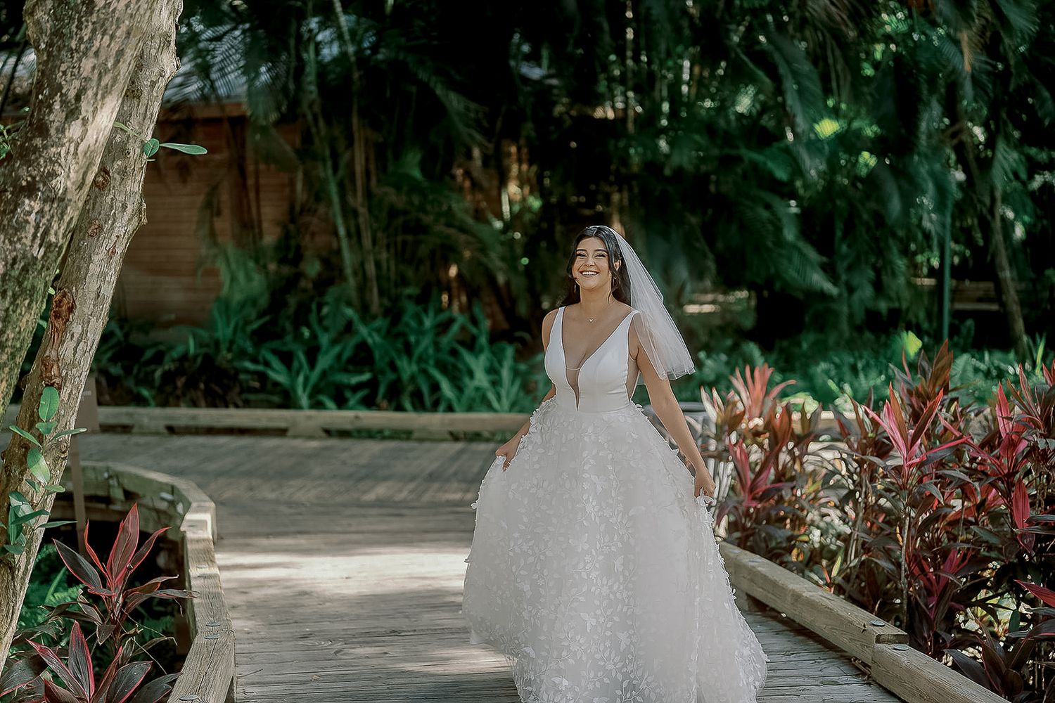 Bride in sparkly ball gown walking on garden path with lush greenery.