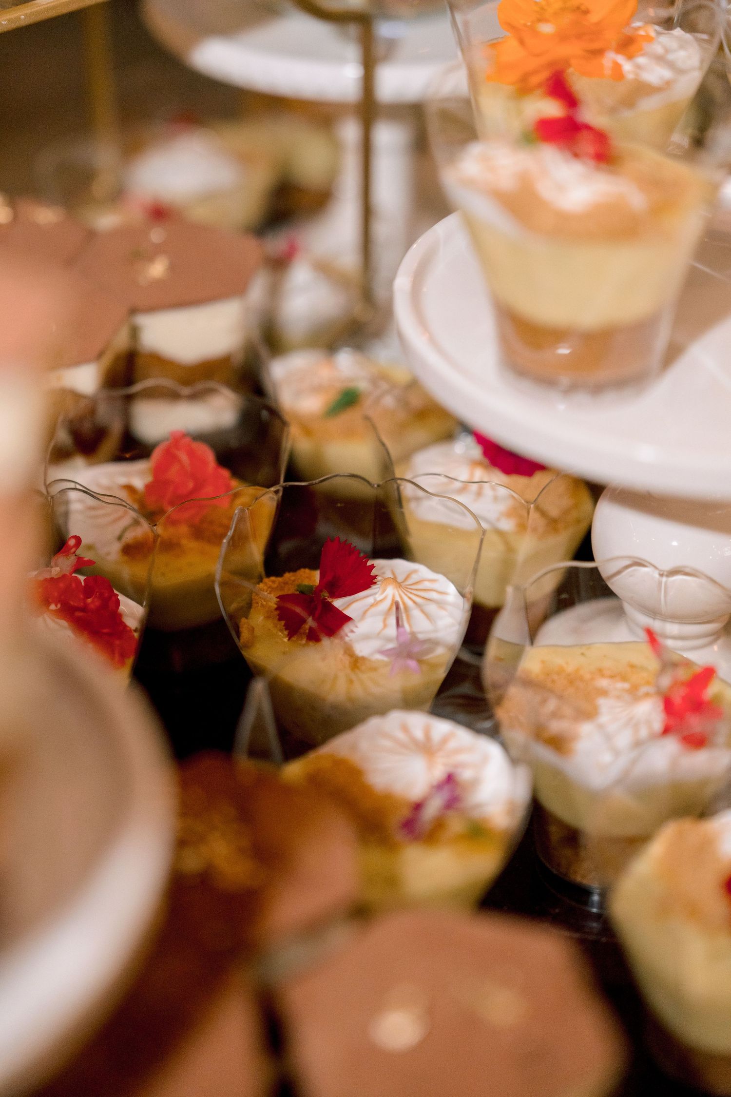Elegant wedding dessert table featuring individual cups with floral garnishes and layered treats on a tiered display stand.