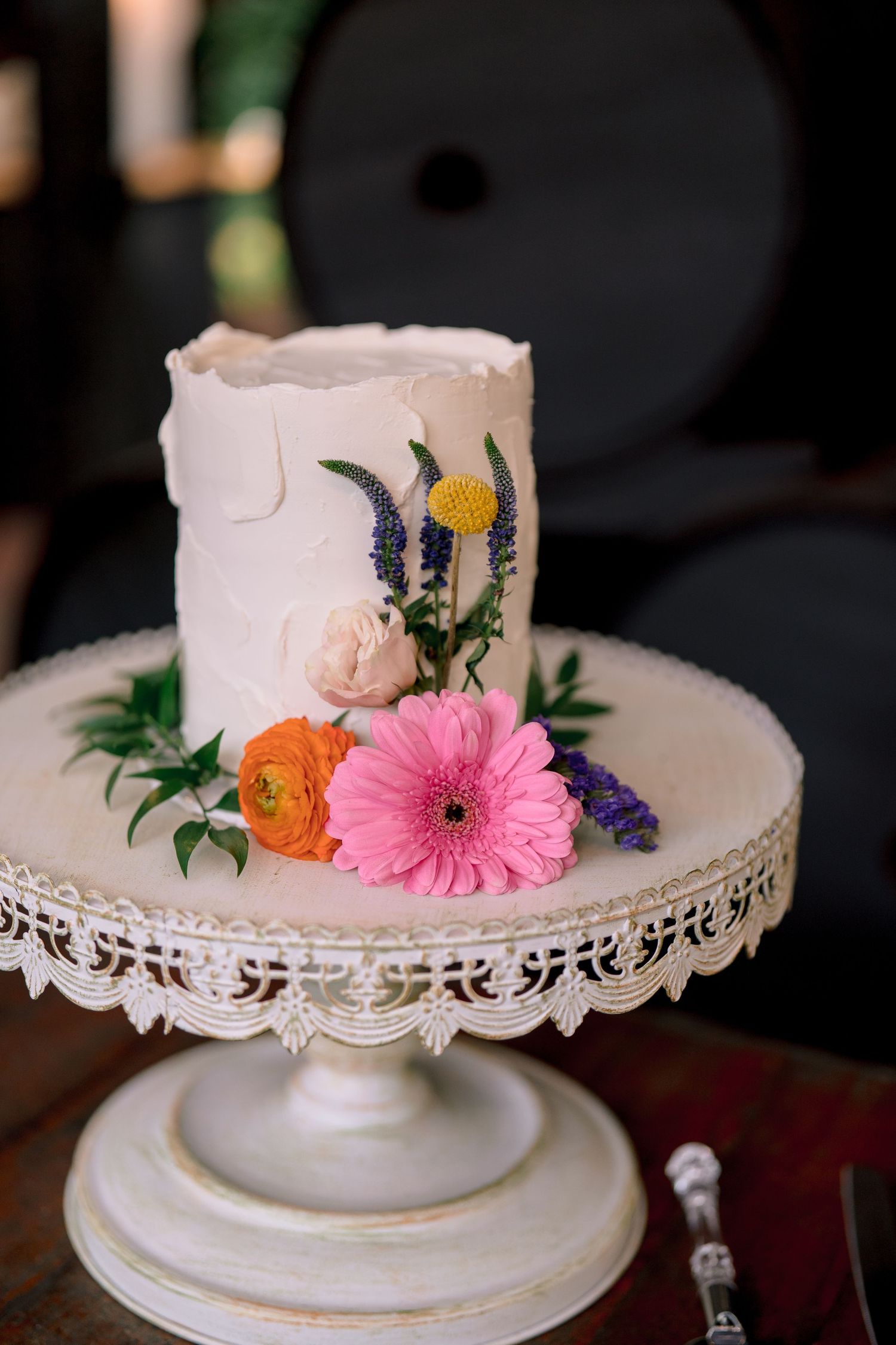 Elegant white wedding cake decorated with colorful fresh flowers on ornate vintage cake stand.