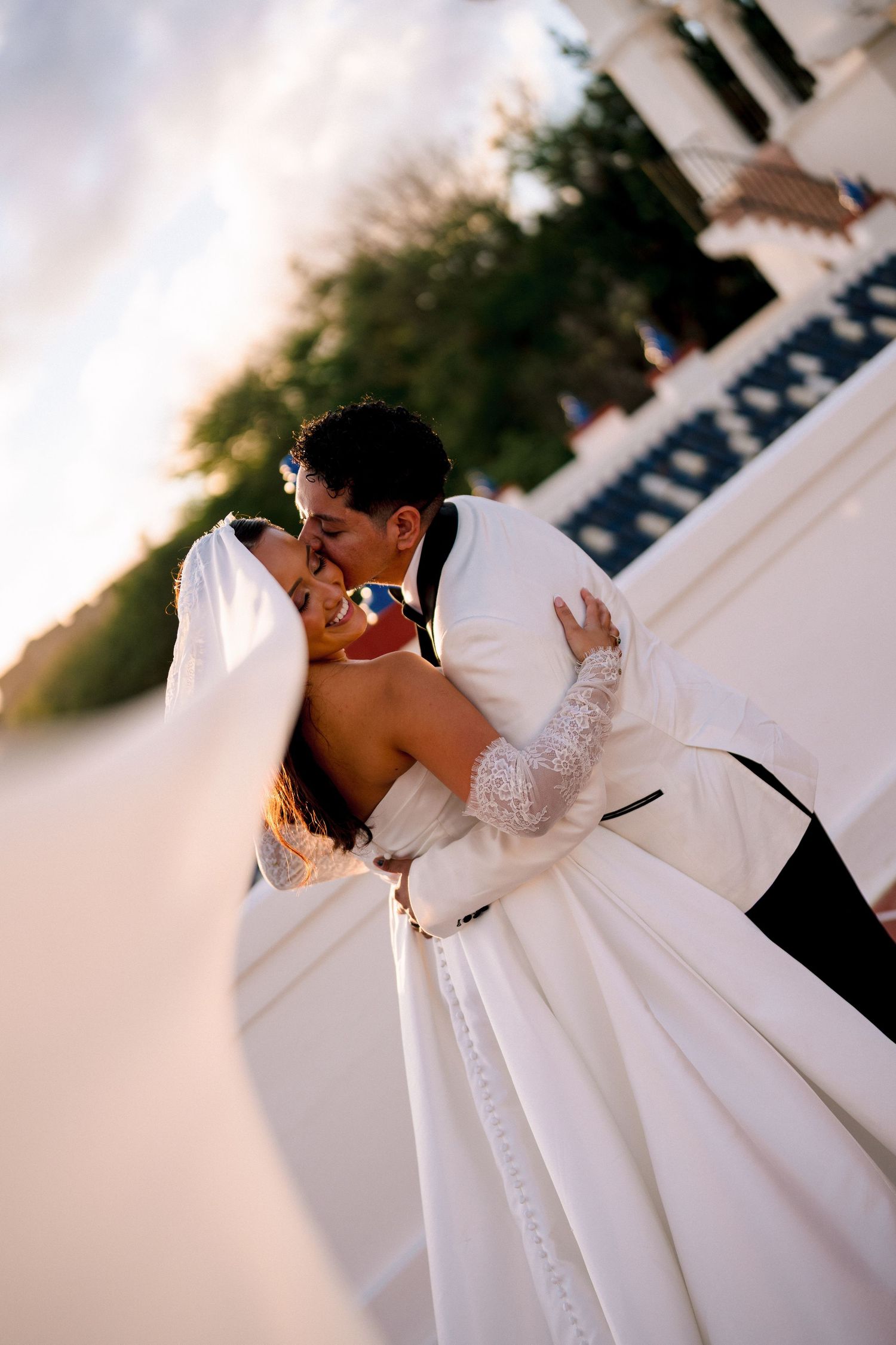 Bride and groom sharing a romantic dip kiss outdoors at golden hour.