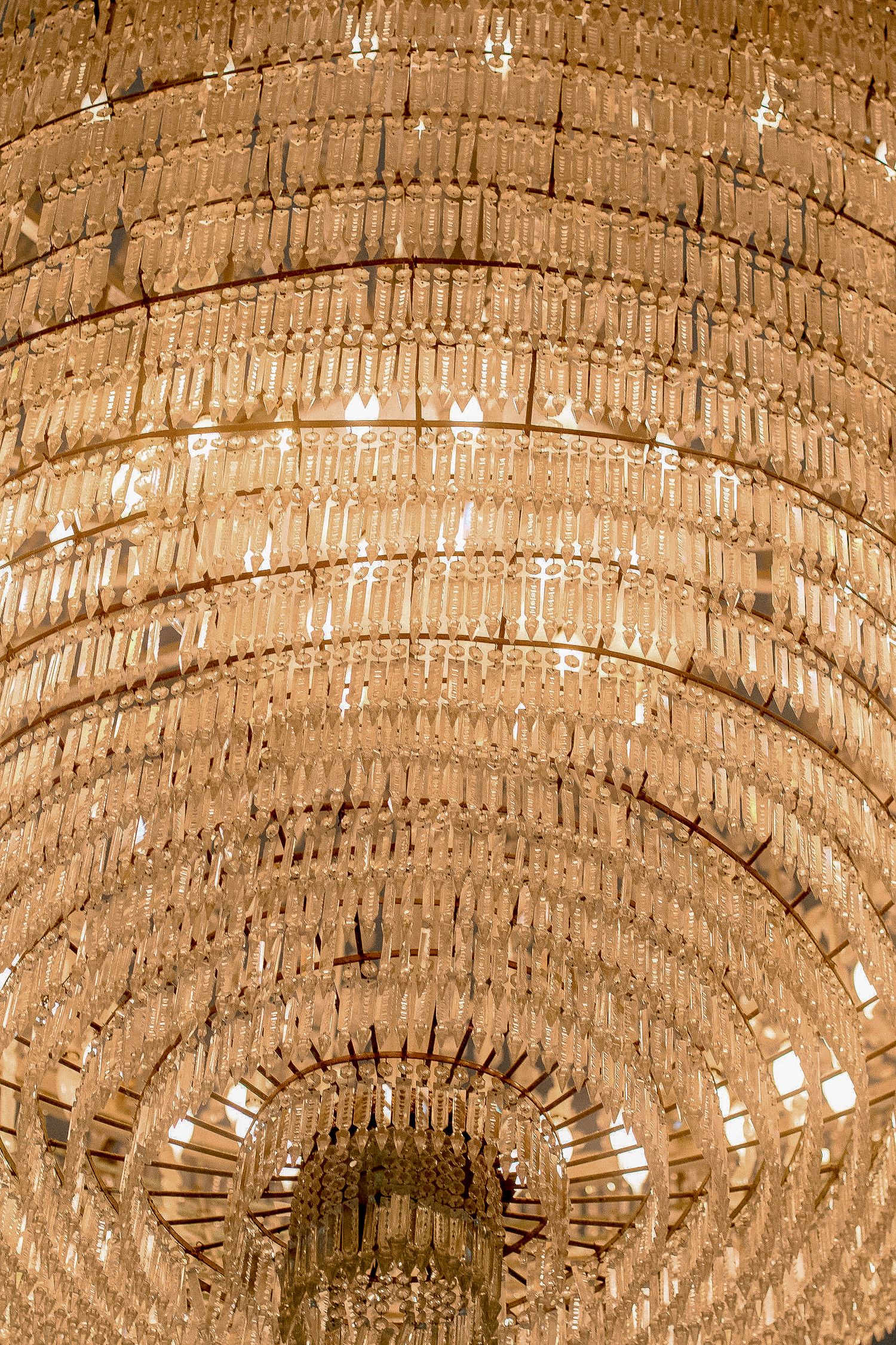 Stunning large crystal chandelier viewed from below, featuring cascading tiers of glass prisms in warm golden light.