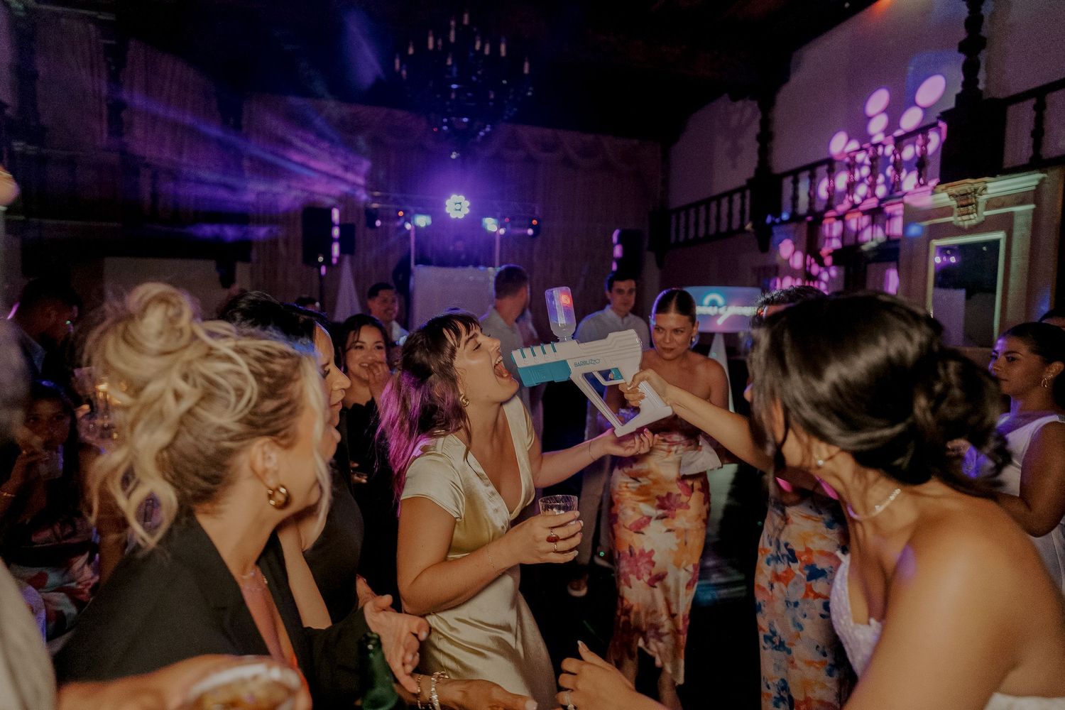 Bride dances joyfully with guests under purple disco lights at vibrant wedding reception party.