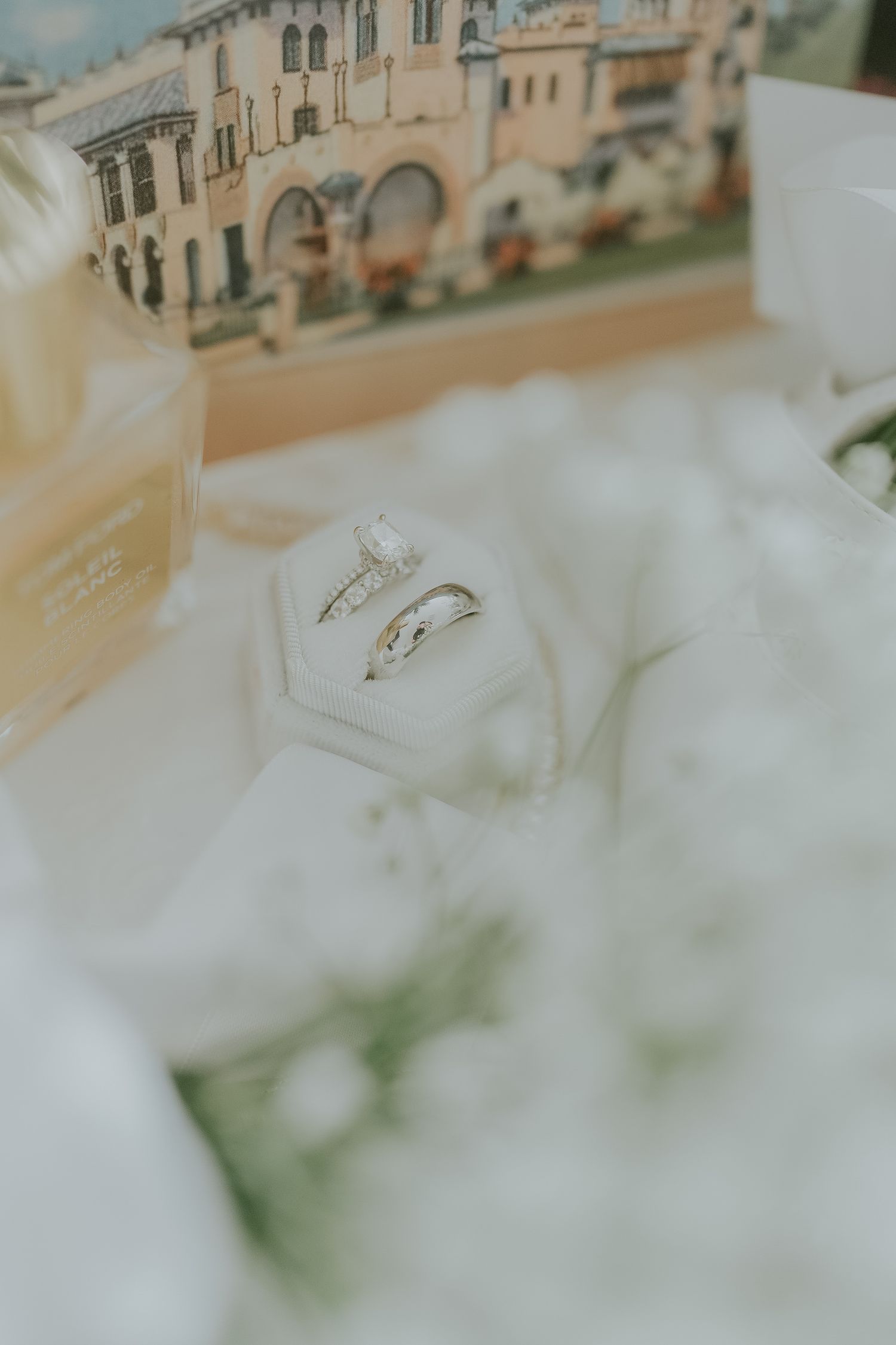 Two wedding rings displayed in a white hexagonal ring box surrounded by white flowers and elegant decor.