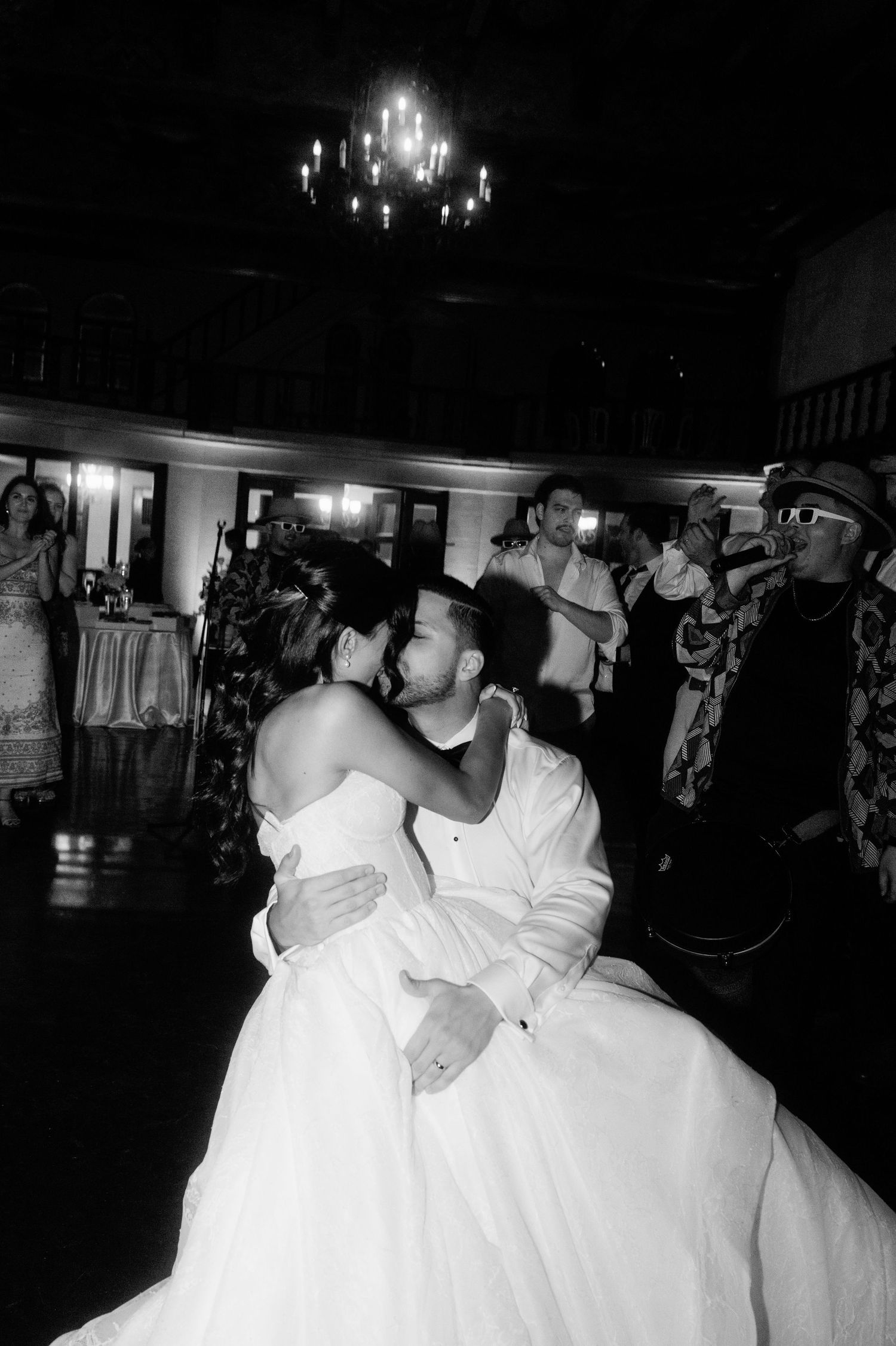 Black and white photo of newlyweds sharing intimate kiss on dance floor at wedding reception.