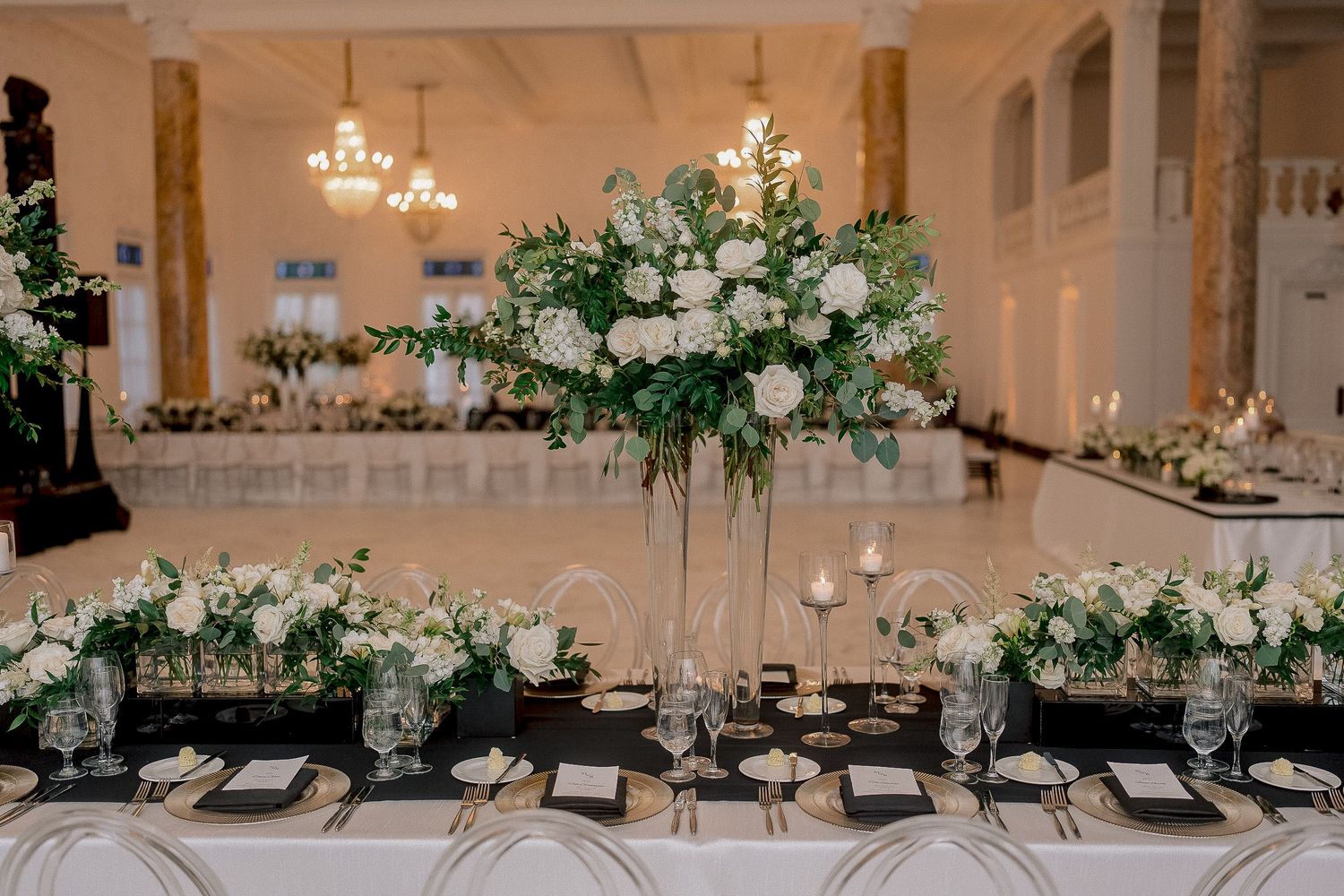 Luxurious wedding reception tablescape with tall white floral centerpieces and black linen accents.