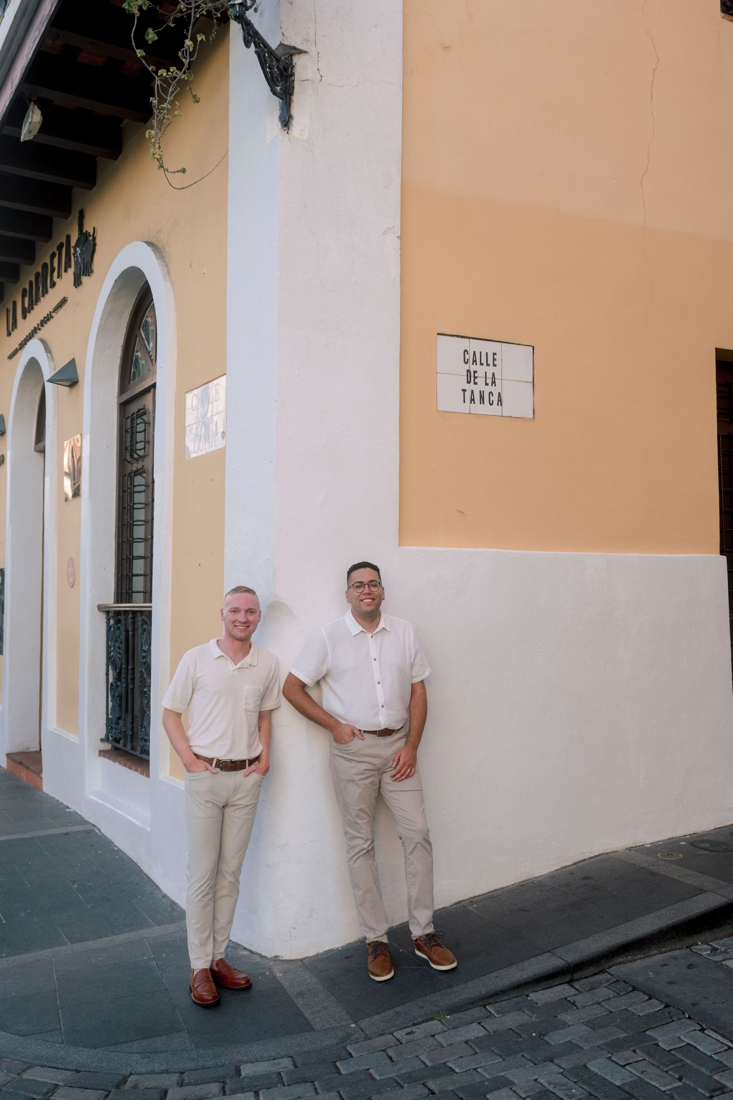 Two men in white shirts and khakis pose on Calle De La Tanca street corner in Old San Juan, Puerto Rico.