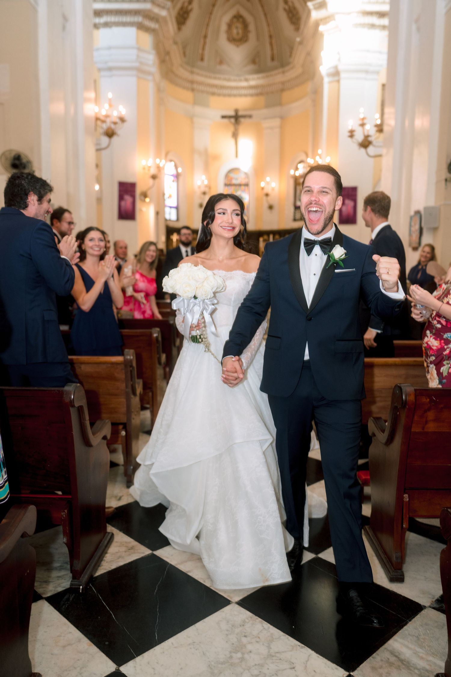 Joyful newlyweds walking down church aisle after wedding ceremony, groom celebrating excitedly.