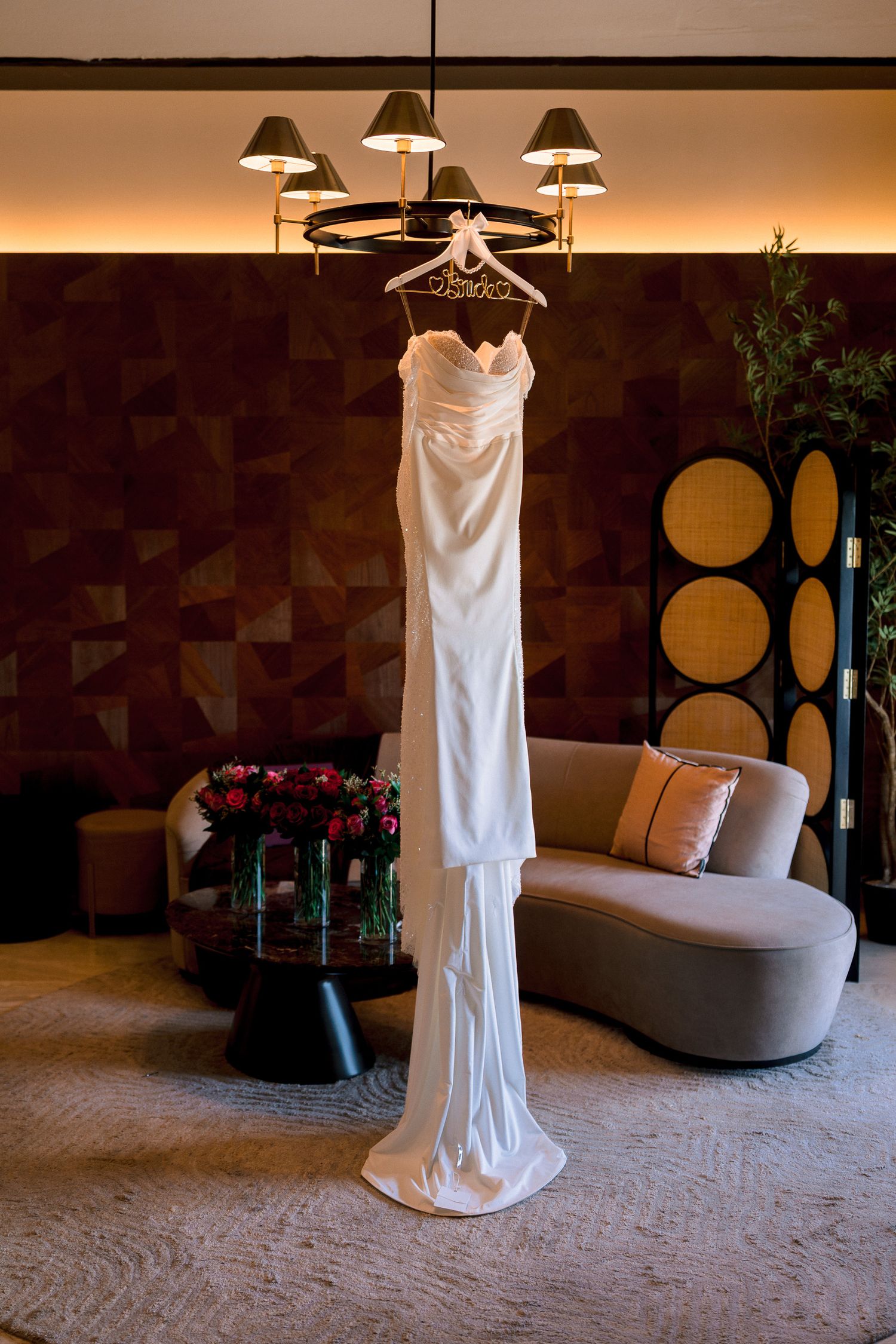 Elegant white wedding dress hanging from a chandelier in a luxurious hotel suite with modern decor.