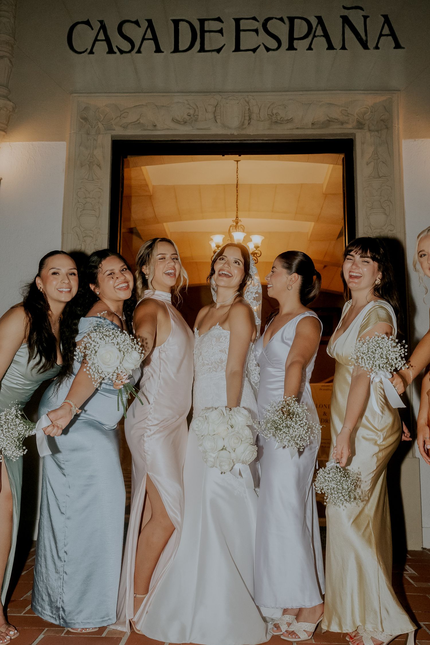 Bride laughs joyfully with bridesmaids in mixed pastel gowns at Casa de España wedding venue.