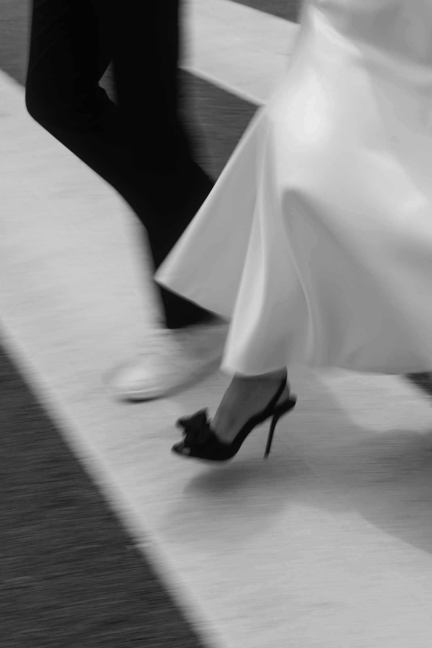 Black and white motion blur photo of a bride in white gown and black heels dancing with a groom in dark suit.