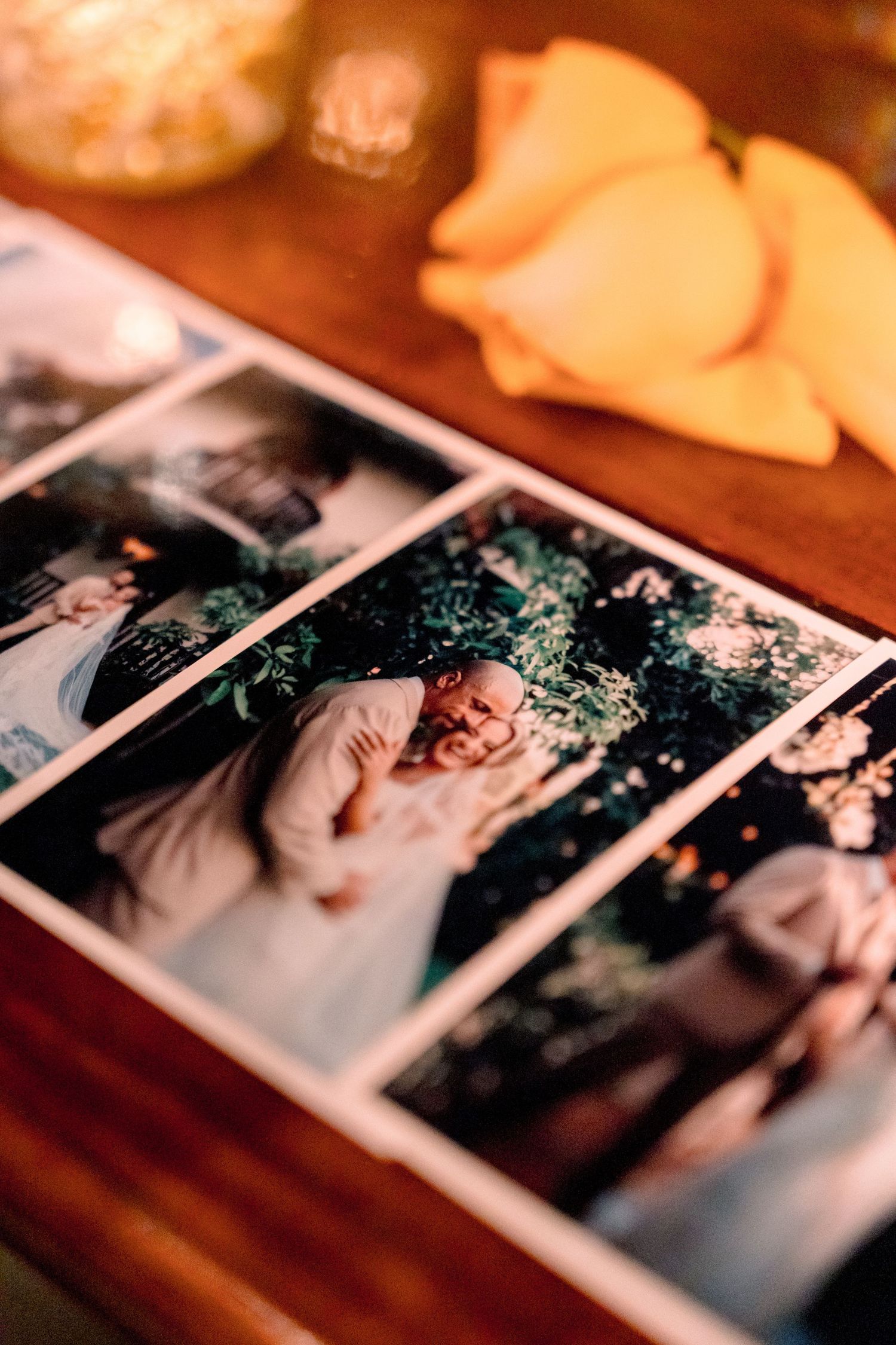 Wedding photo album open on wooden table with rose petals showing couple embracing outdoors.