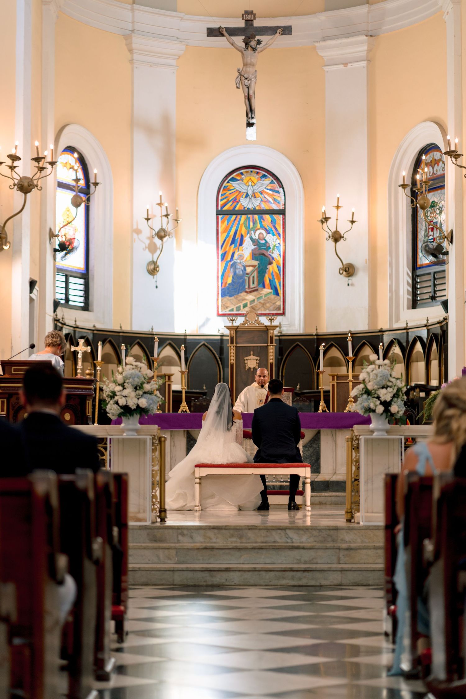 Bride and groom kneeling at church altar during traditional Catholic wedding ceremony.