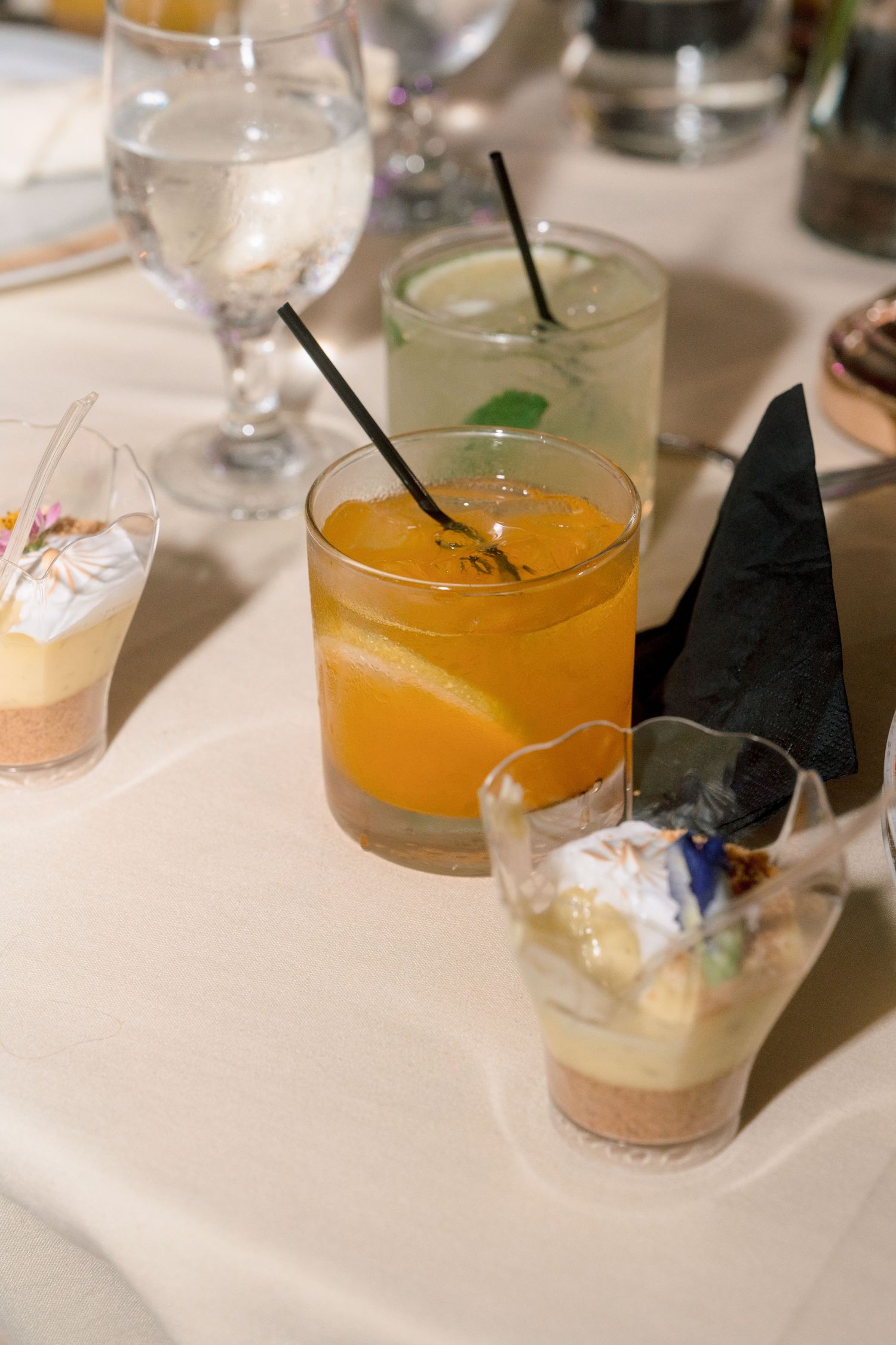 Elegant wedding reception table with an orange cocktail, green drink, water glass, and layered dessert cups.