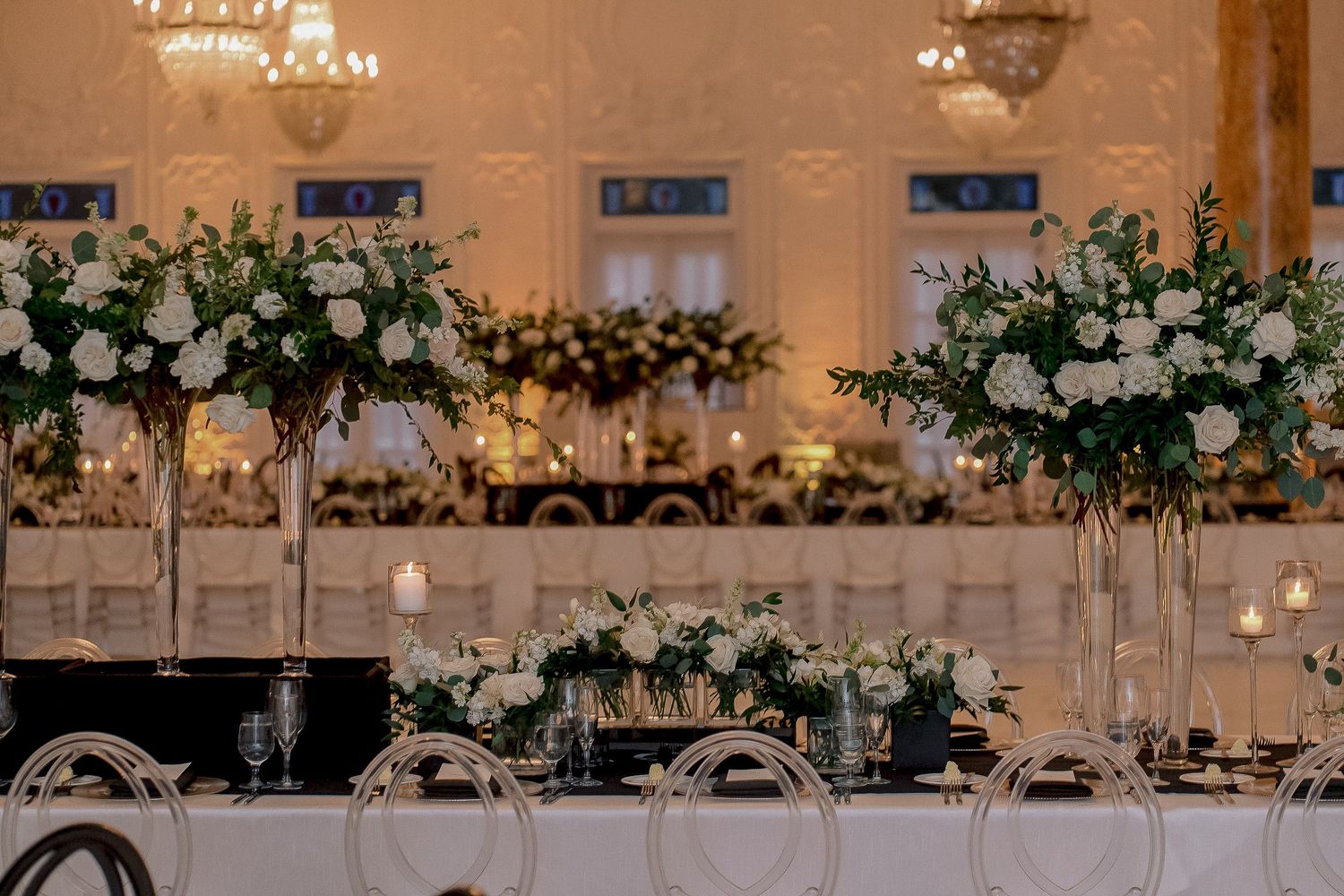 Sophisticated wedding head table with tall white rose centerpieces and candlelit black linen decor.